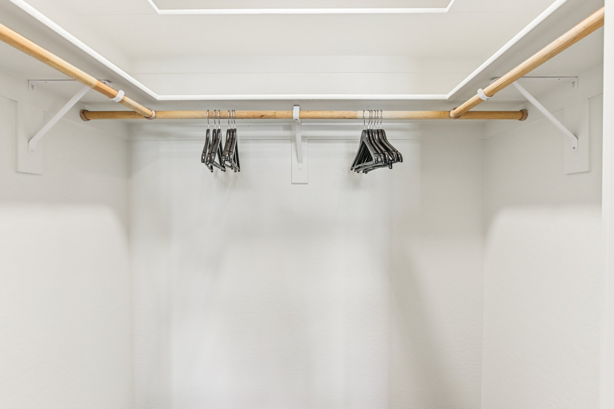 An empty closet with a wooden hanging rod and several black hangers organized on the rod against a white background. The closet appears clean and minimalistic, emphasizing open space and simplicity.
