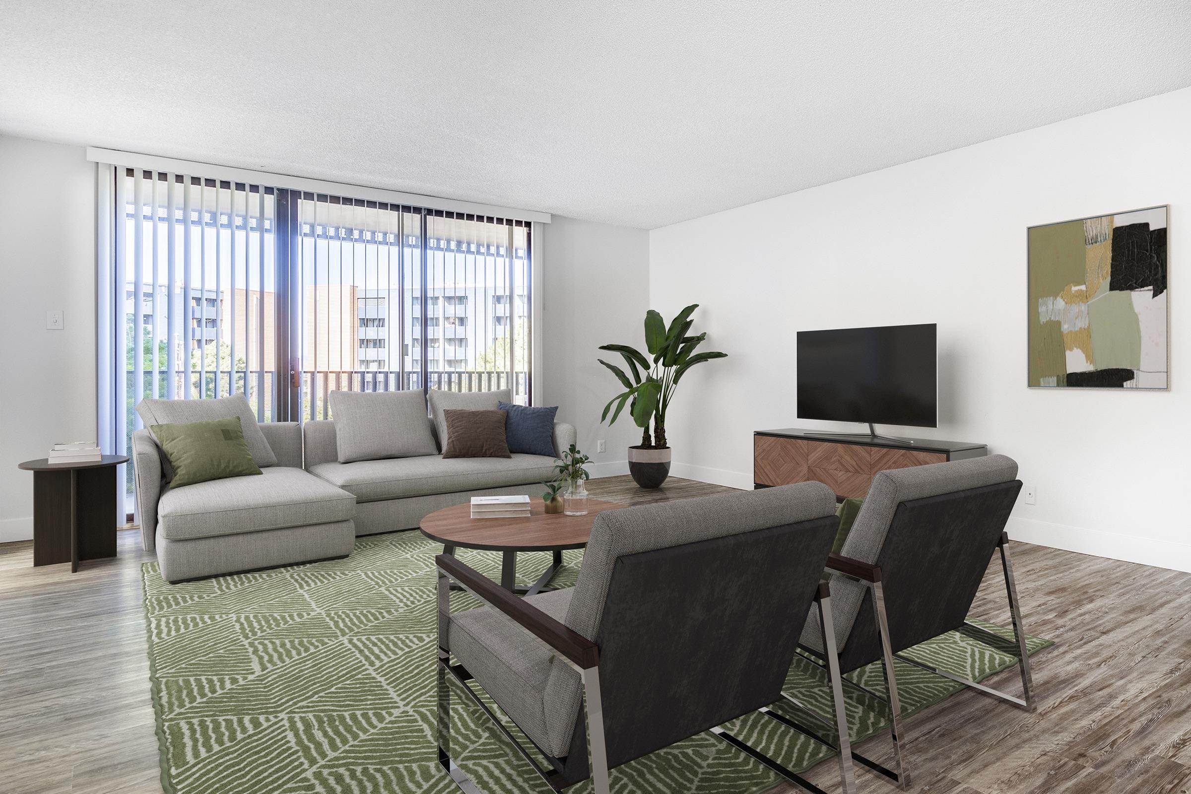 A modern living room featuring a light-colored couch with green accents, two mid-century style chairs, a wooden coffee table, and a flat-screen TV on a stylish cabinet. Large windows with vertical blinds allow natural light, and a potted plant adds greenery to the space.
