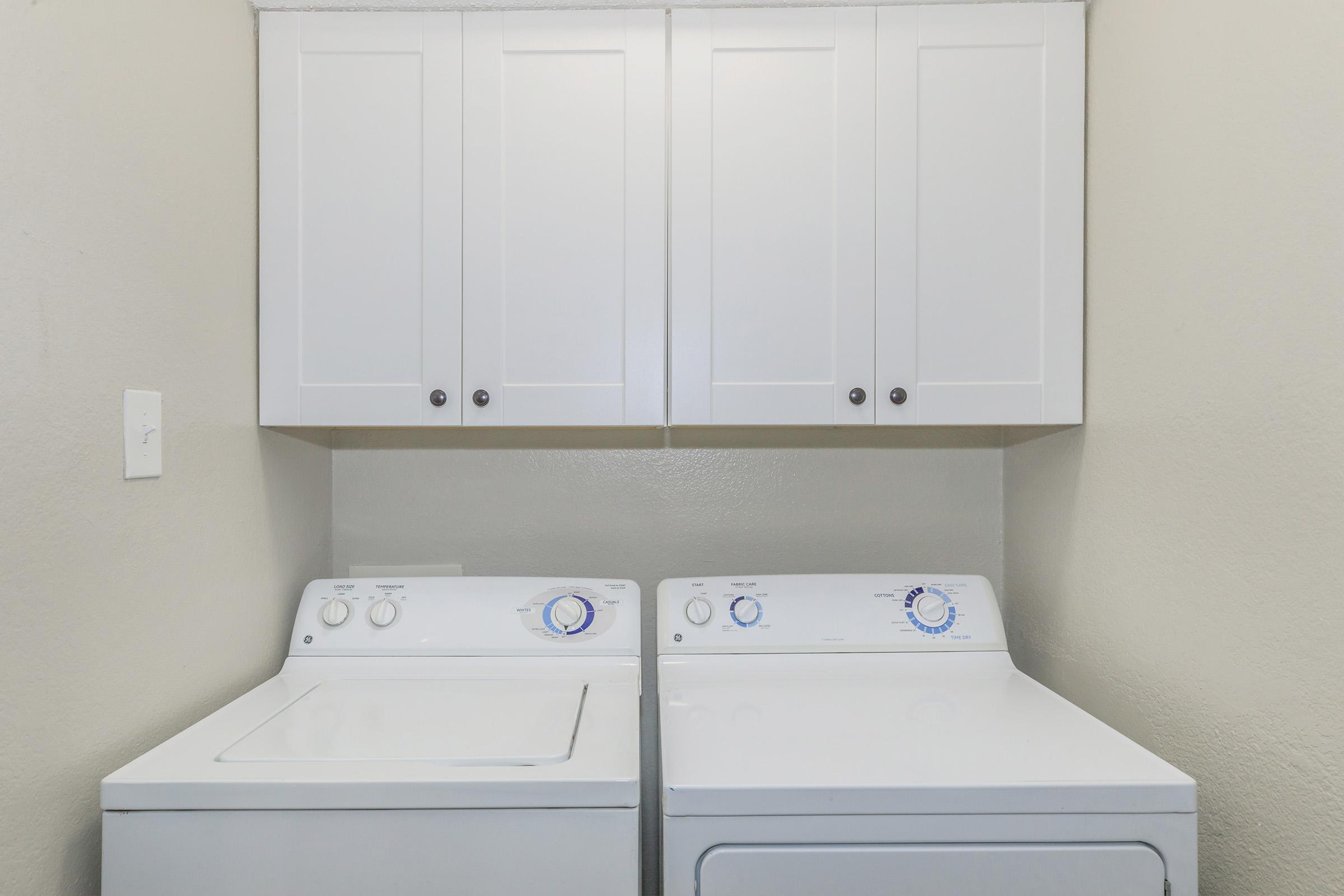 A clean laundry room featuring a stacked washer and dryer side by side, with white cabinetry above. The walls are painted a light color, creating a bright and organized space for laundry tasks.