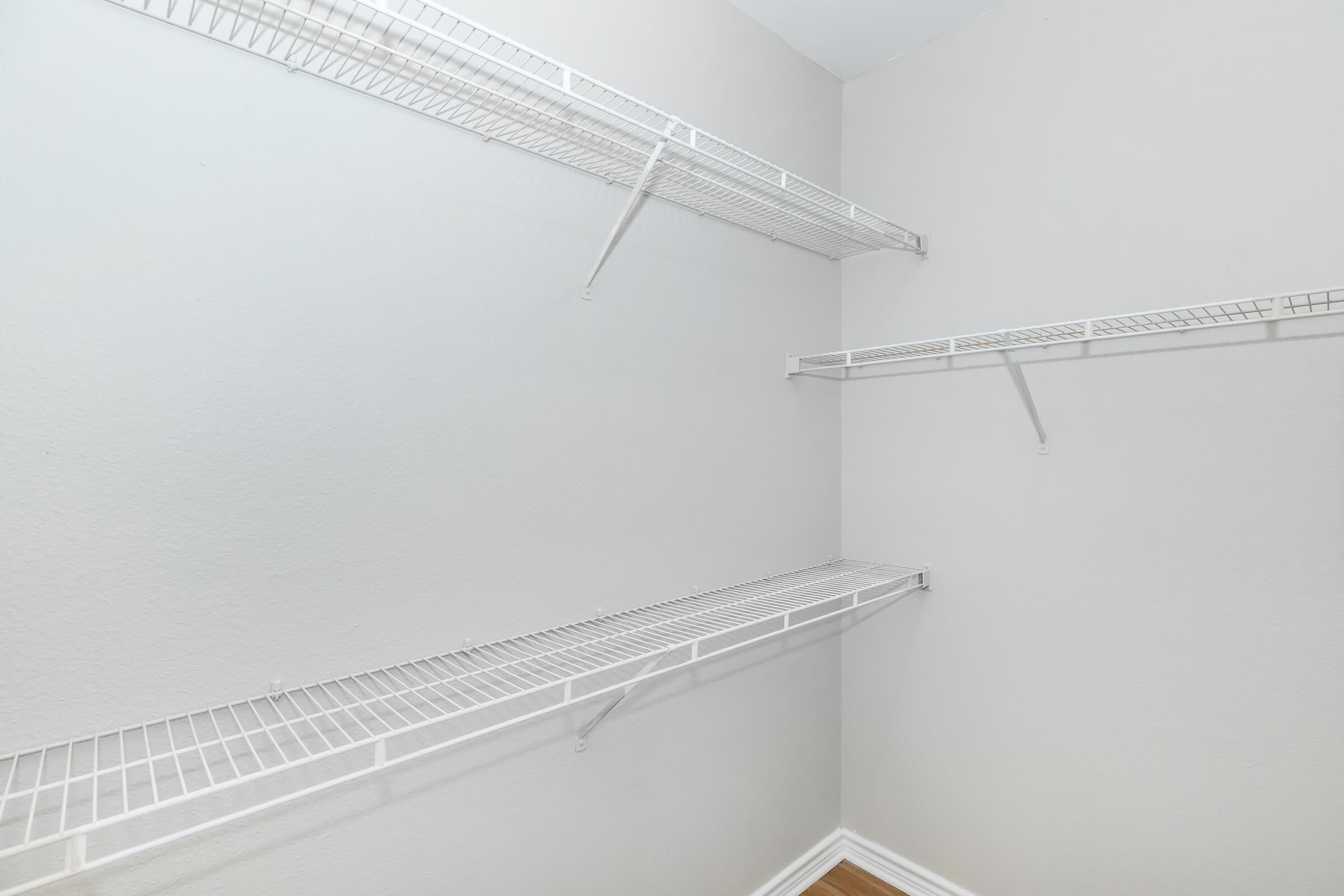 Empty closet with two white wire shelves mounted on light gray walls. The floor is wooden, adding a warm tone to the minimalistic space.
