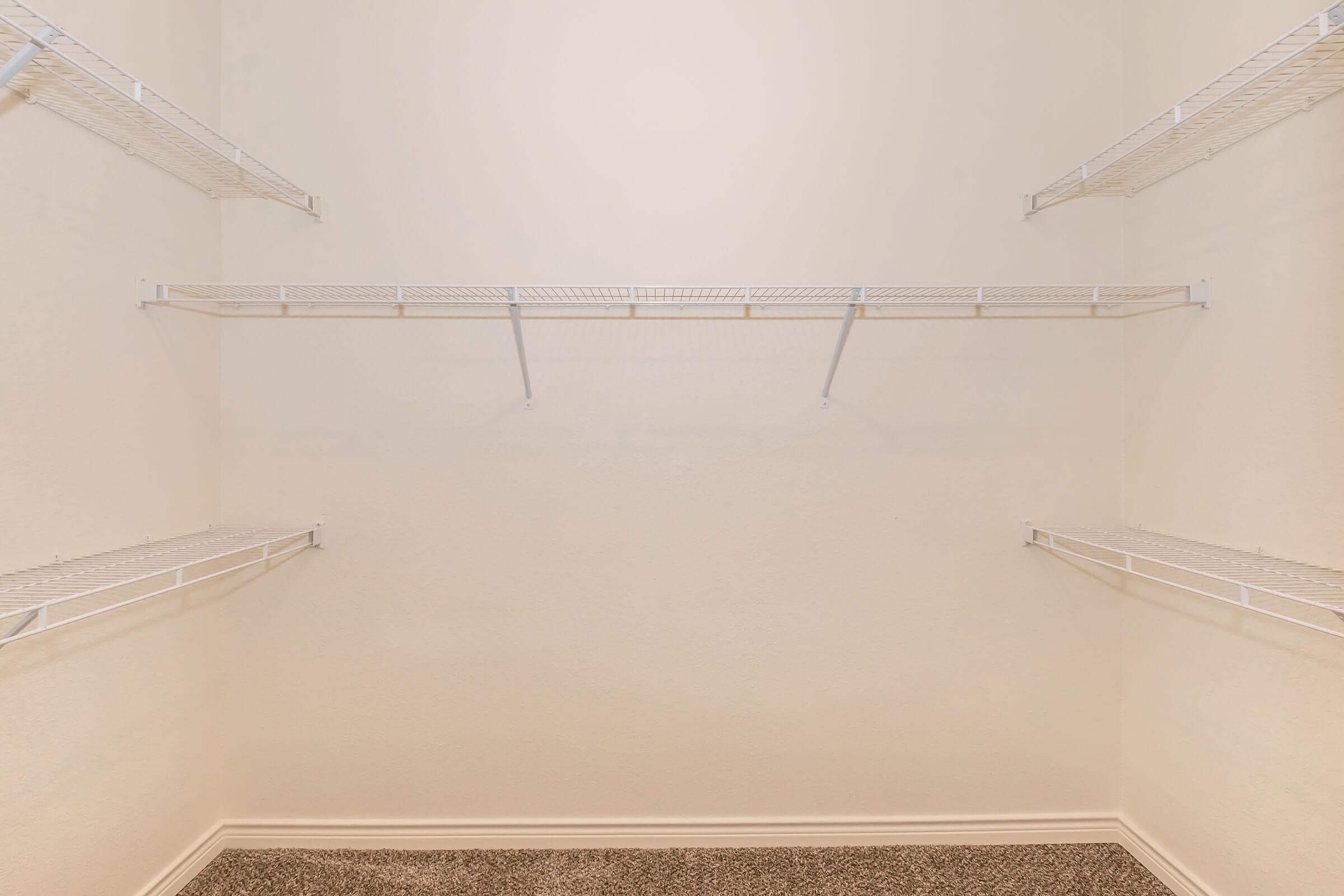 Empty closet with white wire shelving mounted on light-colored walls. The floor is carpeted with a neutral color, and there are no items stored on the shelves, giving it a clean and spacious appearance.