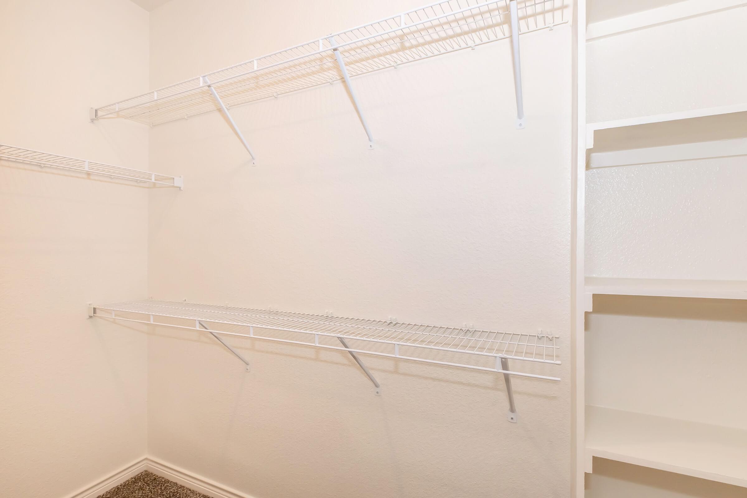 Empty closet interior featuring white wire shelving mounted on light-colored walls. There are three horizontal shelves on one side and a built-in storage space on the other, showcasing minimalistic and organized design. The floor is carpeted.