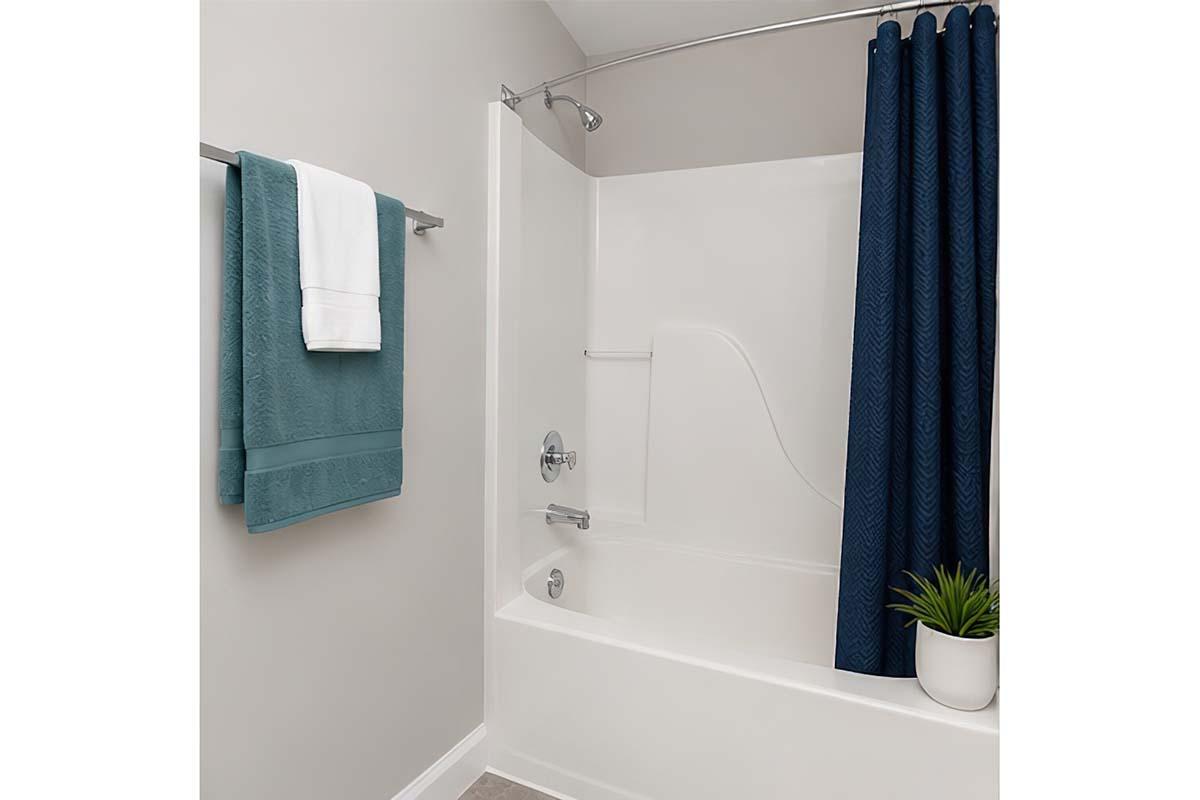 A modern bathroom featuring a white bathtub with a shower, a navy blue shower curtain, a towel rack with folded teal towels, and a potted plant on the edge of the tub. The walls are painted in a neutral color, contributing to a clean and contemporary aesthetic.