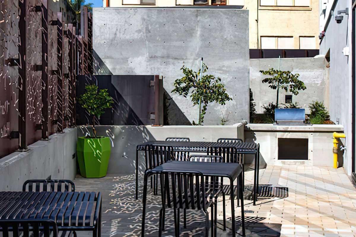 A modern outdoor seating area with black metal tables and chairs arranged on a tiled patio.