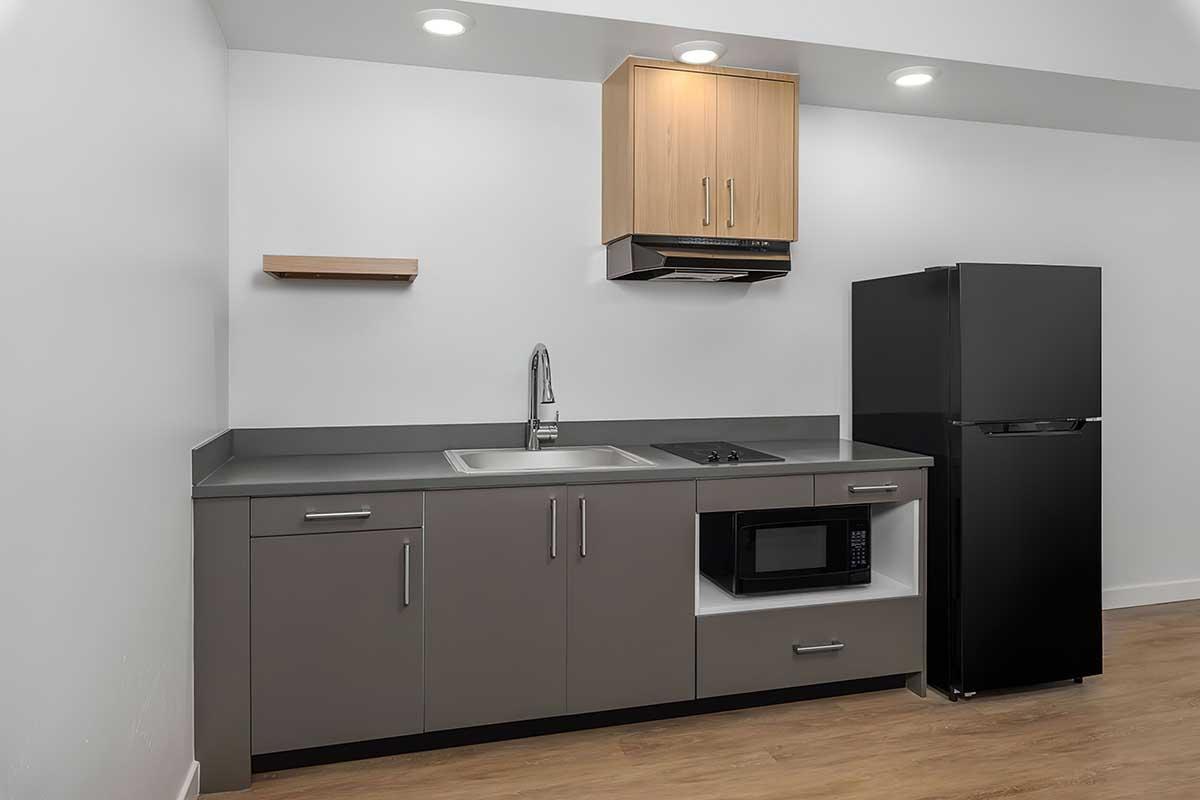 Compact kitchen featuring a stainless steel sink, modern cabinetry in gray and wood finishes, a black refrigerator, and a microwave.