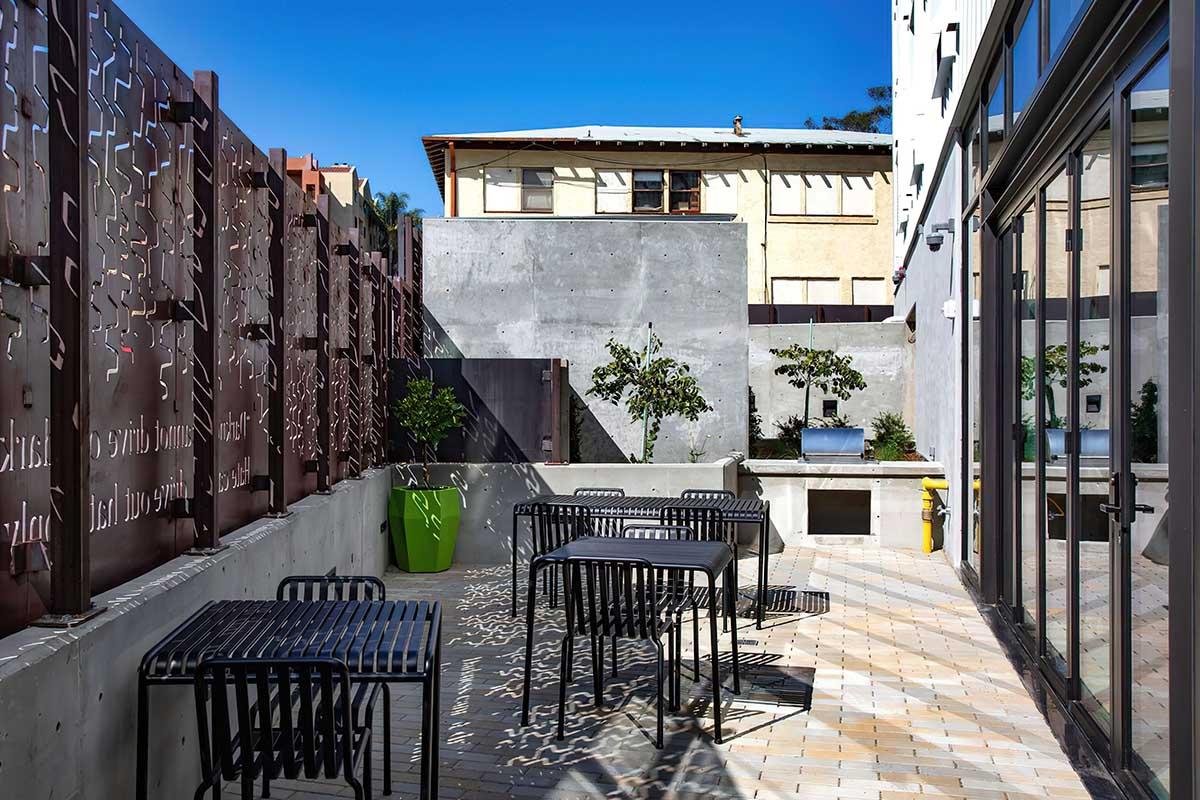 A modern outdoor patio space featuring black metal furniture, including tables and chairs, surrounded by decorative metal panels.