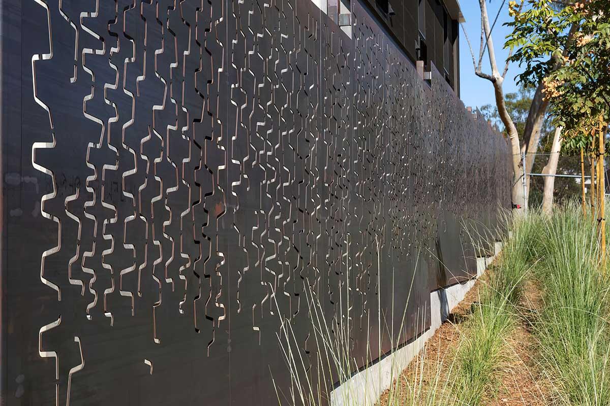 A decorative metal screen with a pattern of wavy, interlocking lines, set against a modern building.
