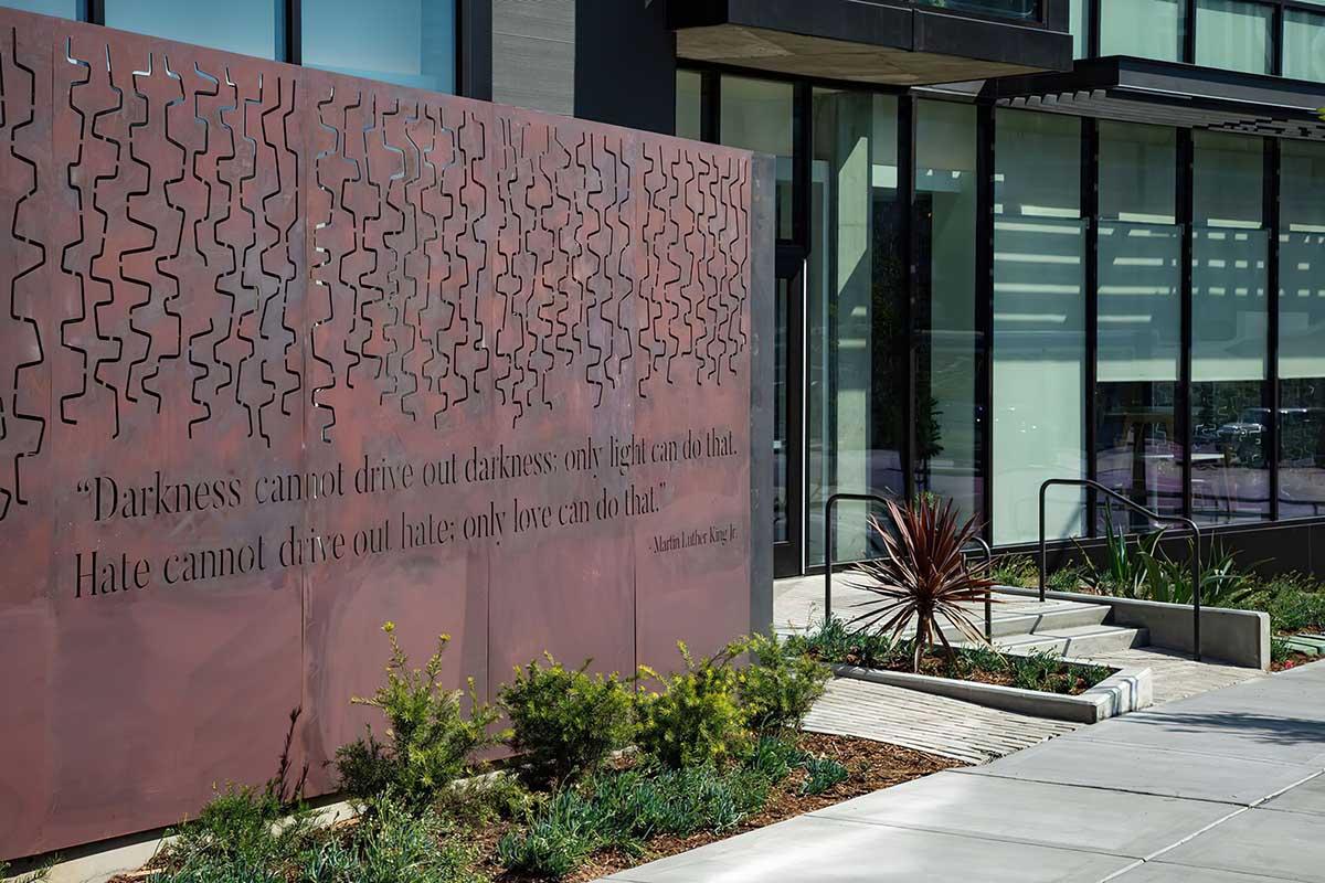 A modern building exterior features a large metal panel with an inspirational quote by Martin Luther King Jr. on it: "Darkness cannot drive out darkness; only light can do that. Hate cannot drive out hate; only love can do that."