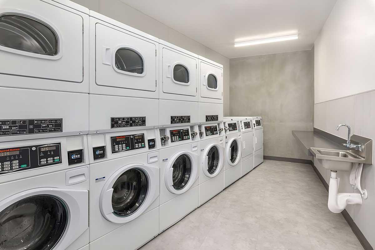 A modern laundromat featuring rows of stacked washing machines and dryers, with a minimalist design.