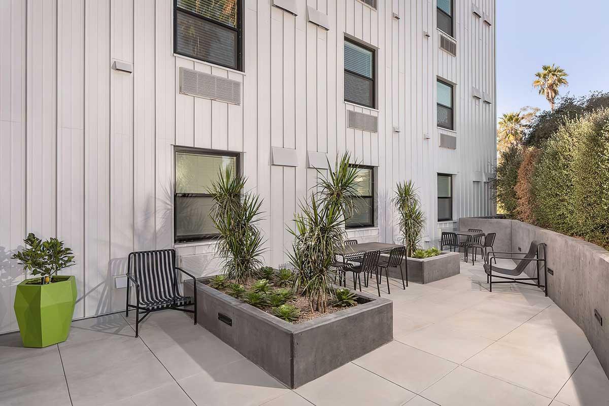 Outdoor patio area featuring concrete planters with greenery, black metal chairs, and a bright green planter.