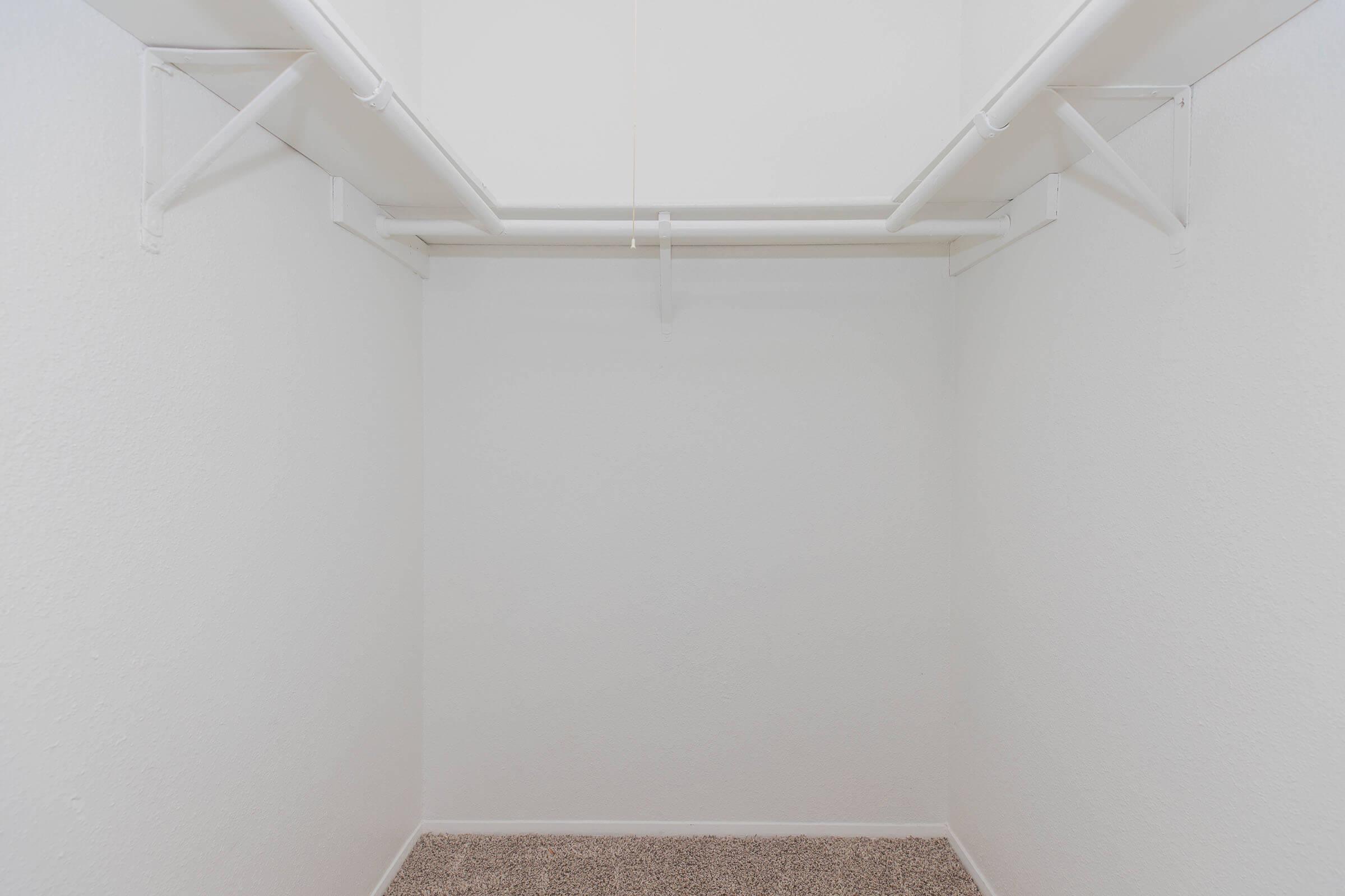 A clean, empty closet with white walls and a light-colored carpet. Two parallel clothes rods are mounted on the walls, providing options for hanging clothes. The space is bright and minimalistic, creating an organized and airy feel.