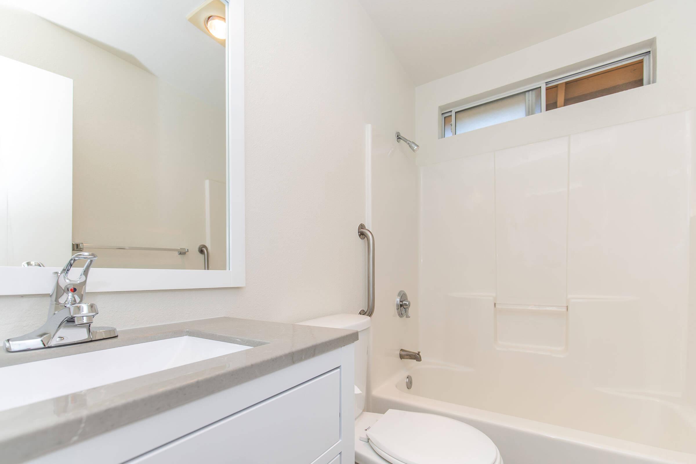 A modern bathroom featuring a clean design with a white bathtub, shower combination, and a sleek vanity with a sink. A mirror hangs above the vanity, and the walls are painted in light colors, creating a bright and spacious feel.