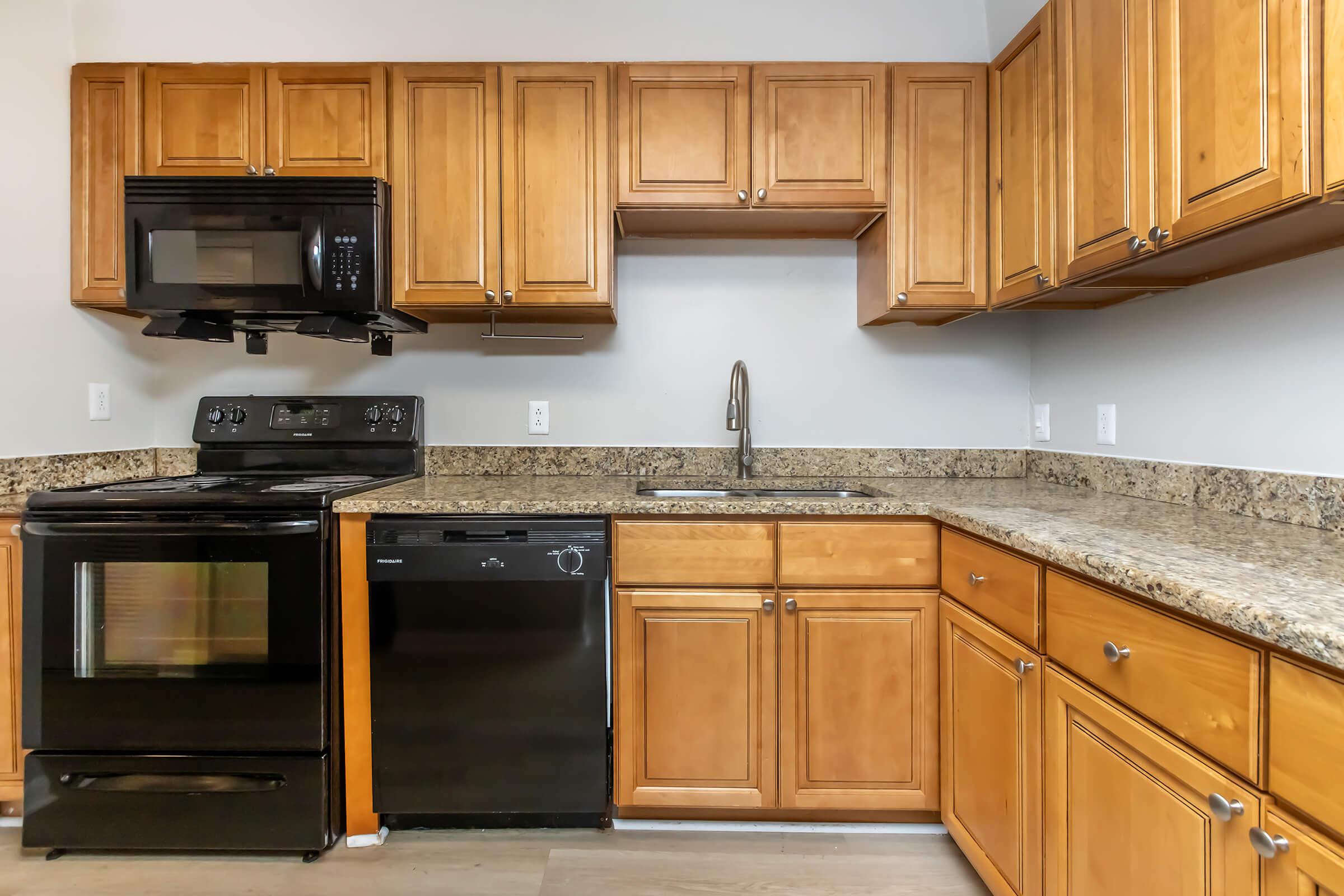 Modern kitchen featuring wooden cabinets, granite countertops, and stainless steel appliances including a microwave, electric stove, and dishwasher. The layout is compact with a sink under a window, offering a clean and functional design.