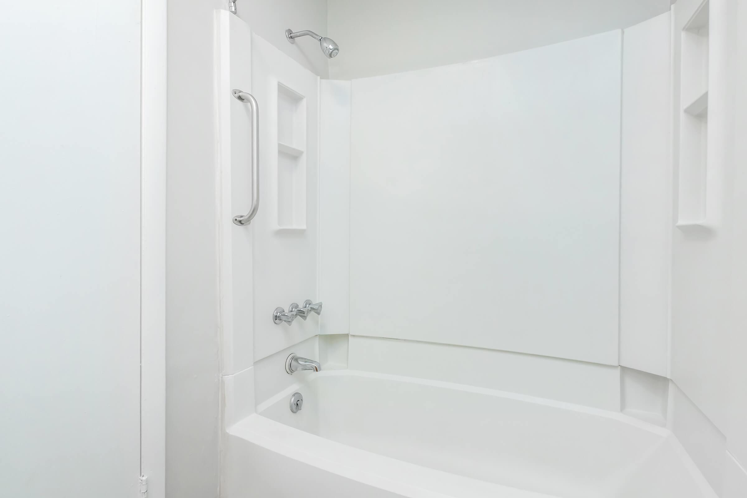 Clean and modern bathroom featuring a white bathtub with a curved shower wall, chrome fixtures, and built-in soap shelves. The overall design is minimalistic and bright, showcasing a simple aesthetic for a relaxing bathing space.