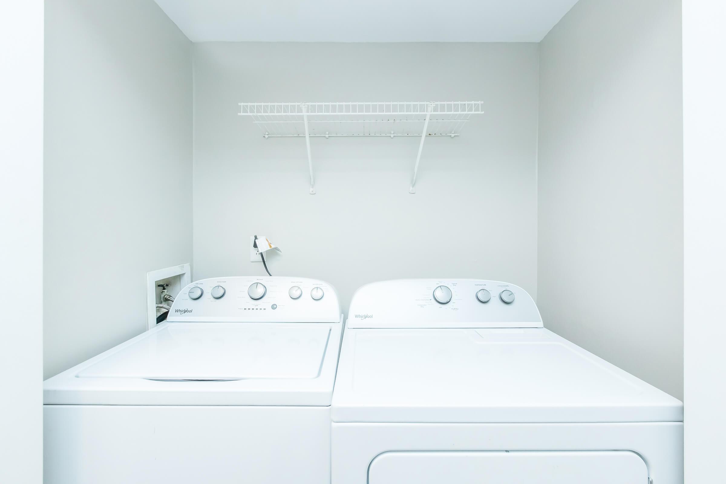 A clean laundry room featuring a white washer and dryer side by side, with a wall-mounted shelf above. The walls are painted in a light color, creating a bright and tidy atmosphere.