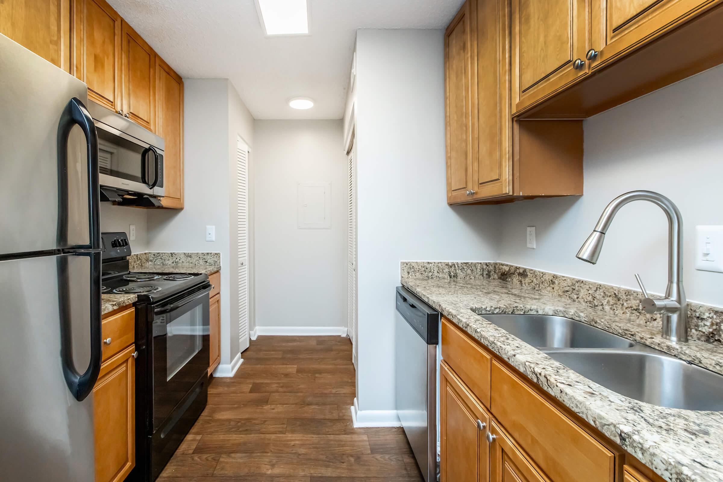 A modern kitchen featuring wooden cabinets, granite countertops, stainless steel appliances including a microwave, oven, and dishwasher. The space has a washer and dryer closet, ample lighting, and a clean design with a neutral color palette and hardwood flooring.