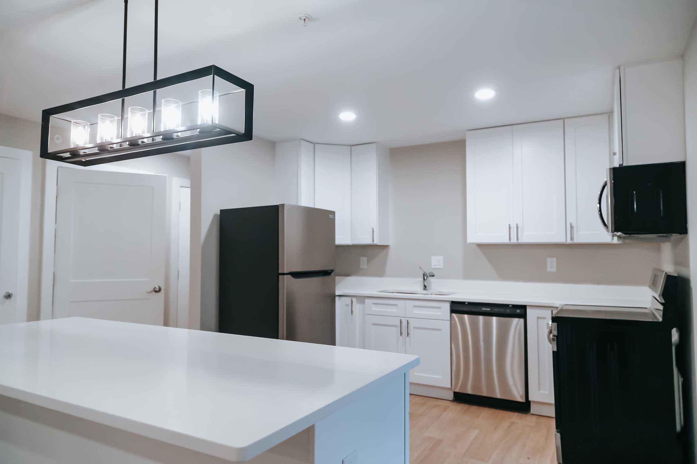 Modern kitchen featuring white cabinets, stainless steel appliances including a refrigerator, microwave, and dishwasher, along with a center island and a stylish pendant light above.