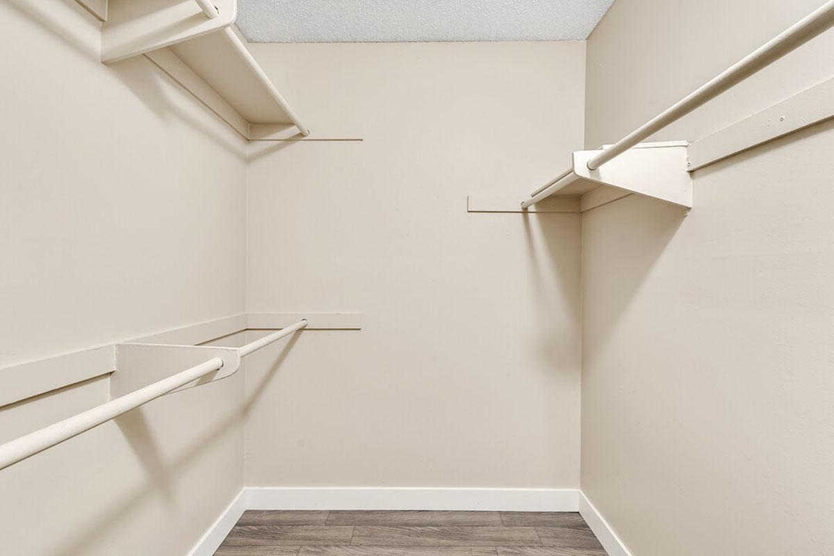 An empty walk-in closet with beige walls, featuring a wooden floor and two hanging rods on opposite walls, providing a spacious and minimalist storage area.