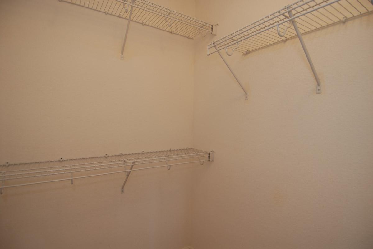 Empty closet with beige walls and metal wire shelving. The shelves are positioned at various heights, providing space for storage. The overall look is clean and uncluttered, highlighting the storage potential of the space.