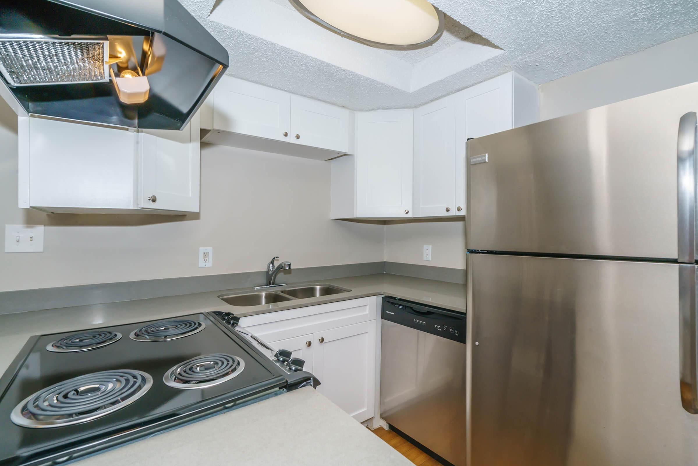 A modern kitchen featuring white cabinetry, a stainless steel refrigerator, a black stove with four burners, a built-in dishwasher, and a double sink. The room has a light ceiling and is designed with neutral colors, providing a clean and functional cooking space.