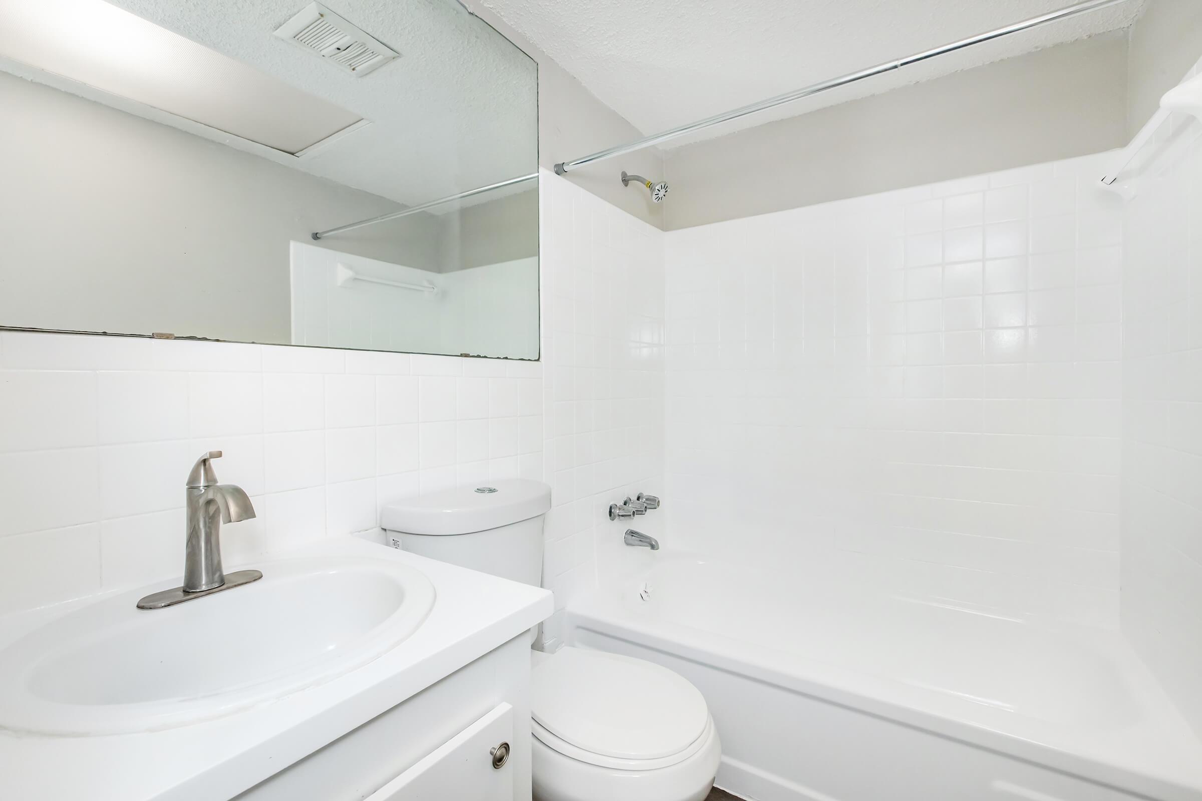 A clean, modern bathroom featuring a white bathtub, toilet, and sink. The walls are tiled, and there is a large mirror above the sink. Soft lighting illuminates the space, creating a bright and inviting atmosphere.