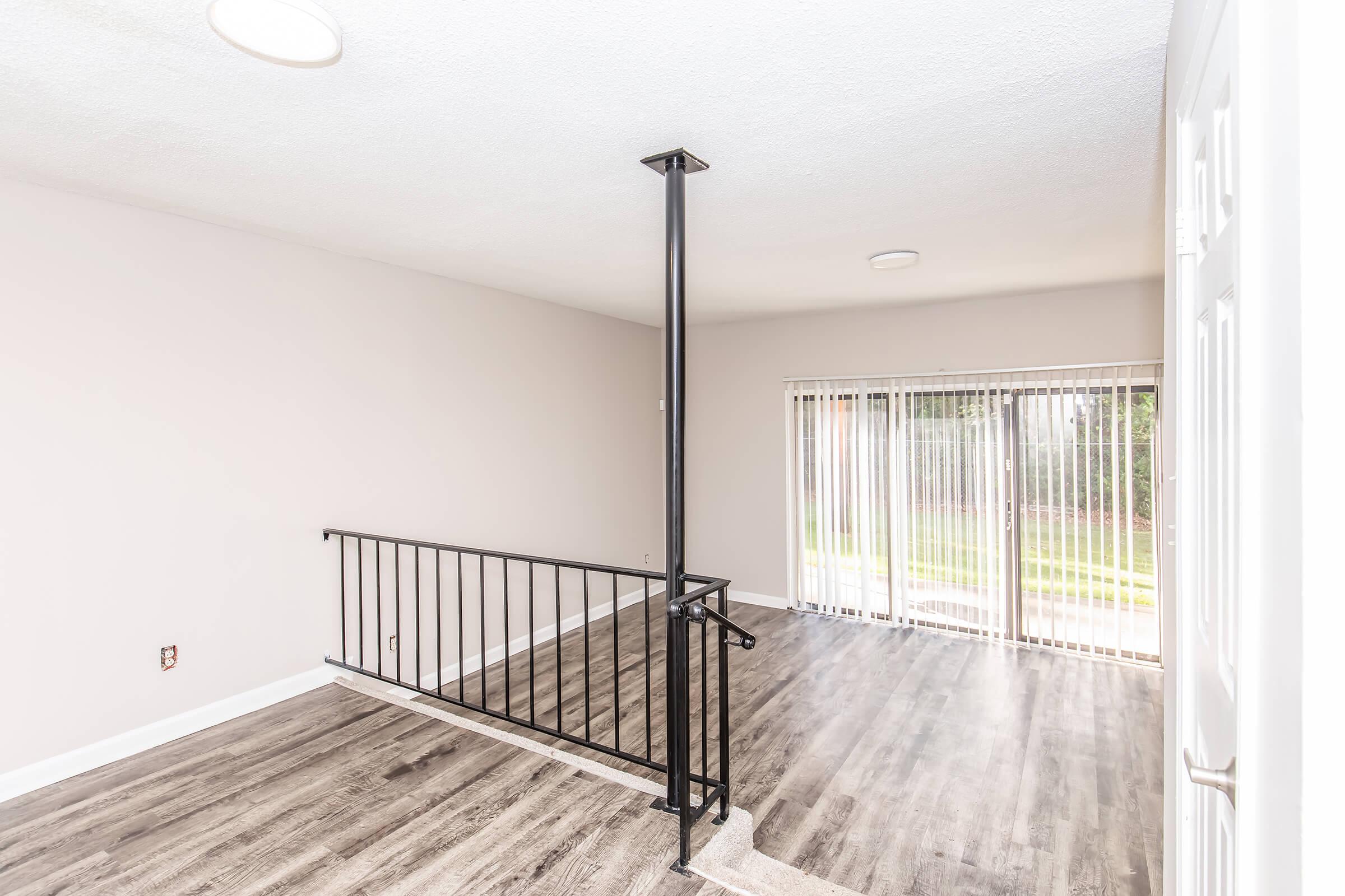 Interior view of a spacious, light-filled area featuring neutral walls, modern flooring, and a sleek black railing. Large sliding glass doors lead to an outdoor space, allowing natural light to fill the room. The design is minimalist and contemporary, creating a welcoming atmosphere.