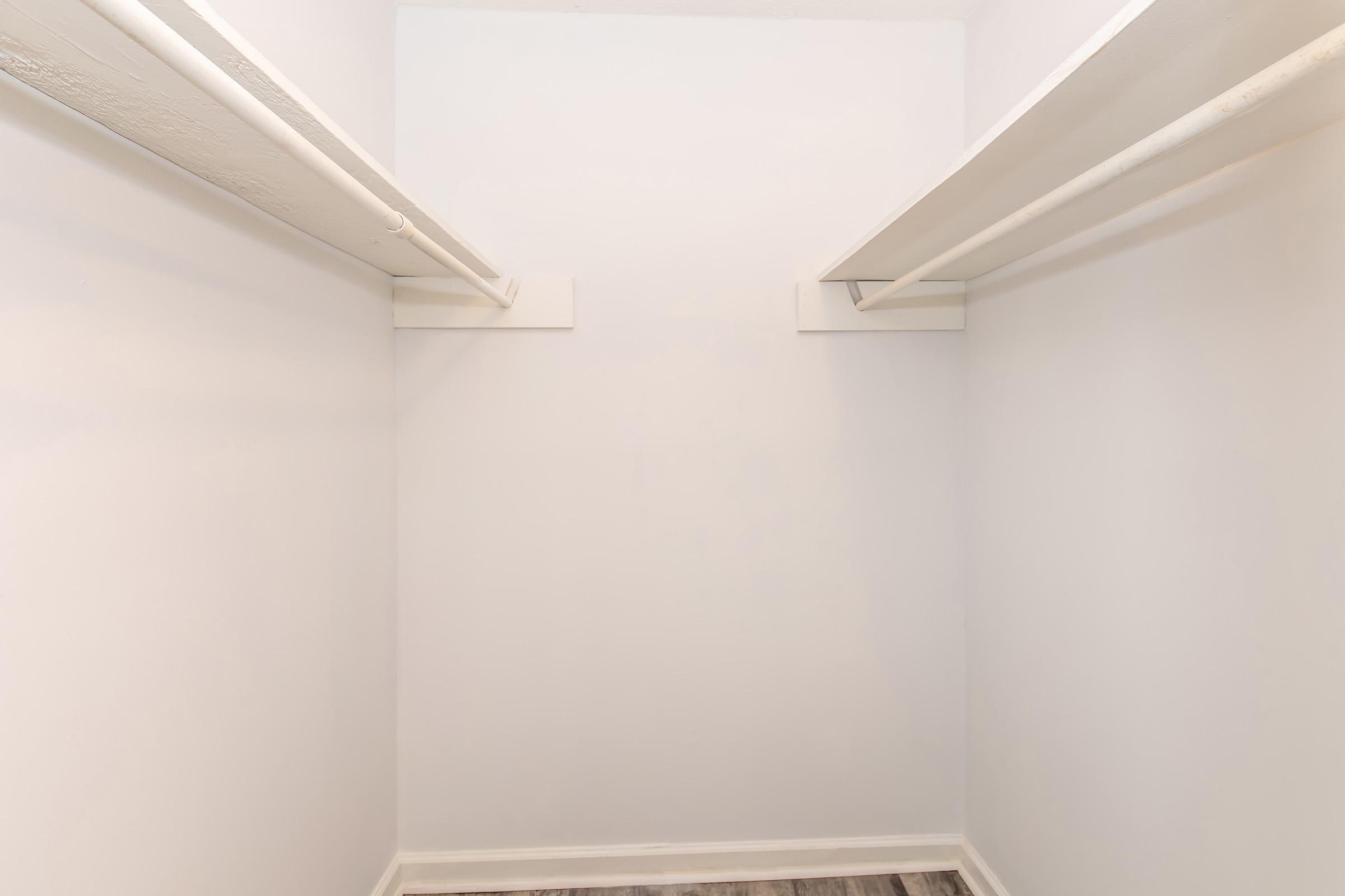 Empty closet with white walls and two horizontal hanging rods. The floor is covered with wood-like laminate, providing a modern touch.