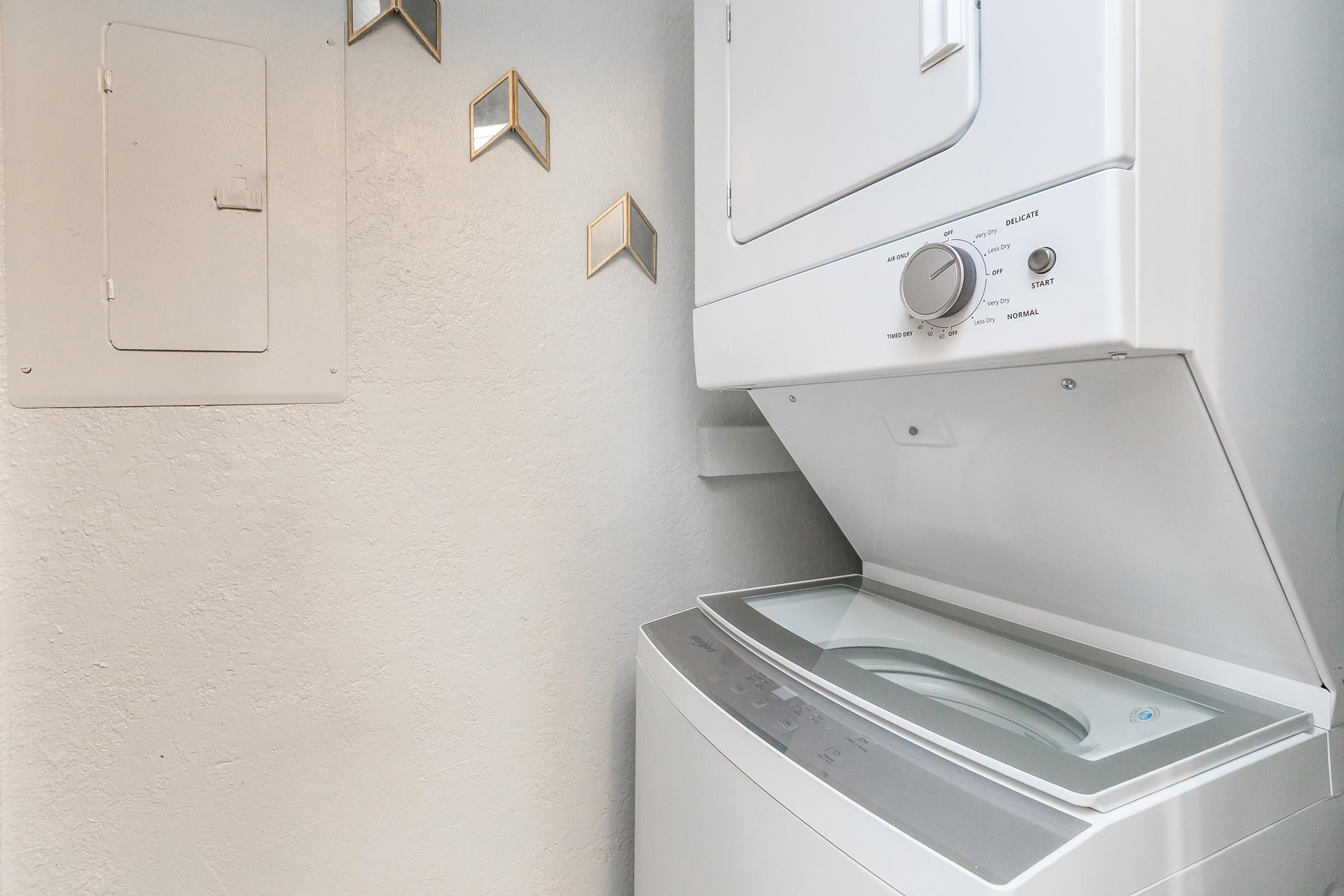 A compact laundry area featuring a stacked washer and dryer unit. The washer is located at the bottom, while the dryer is on top. The walls are painted in a light color, and there are decorative geometric wall accents nearby.