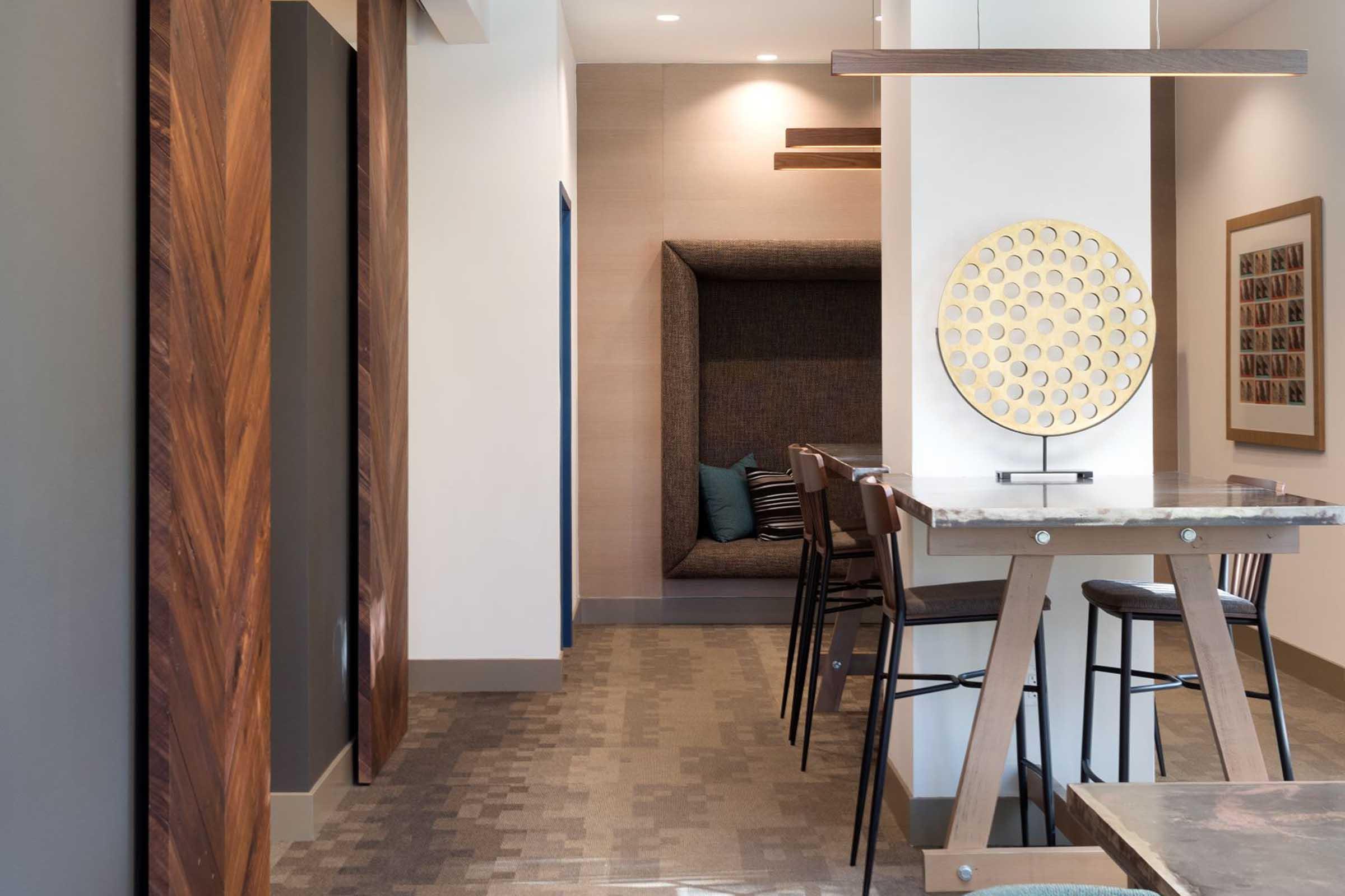 A modern interior space featuring a cozy nook with plush seating, sleek wooden furniture, a stylish circular artwork on the wall, and a neutral color palette. The area has a clean, contemporary design with natural light enhancing the ambiance.