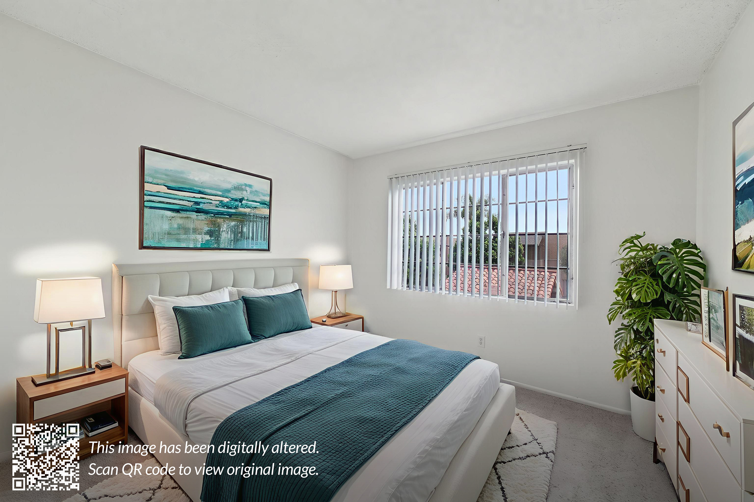 A cozy bedroom featuring a queen-sized bed with teal accent pillows and a light comforter. There's a modern headboard, two bedside lamps, and a dresser. A large window with white blinds lets in natural light, and a piece of wall art adds a decorative touch. The room has a clean, inviting atmosphere.