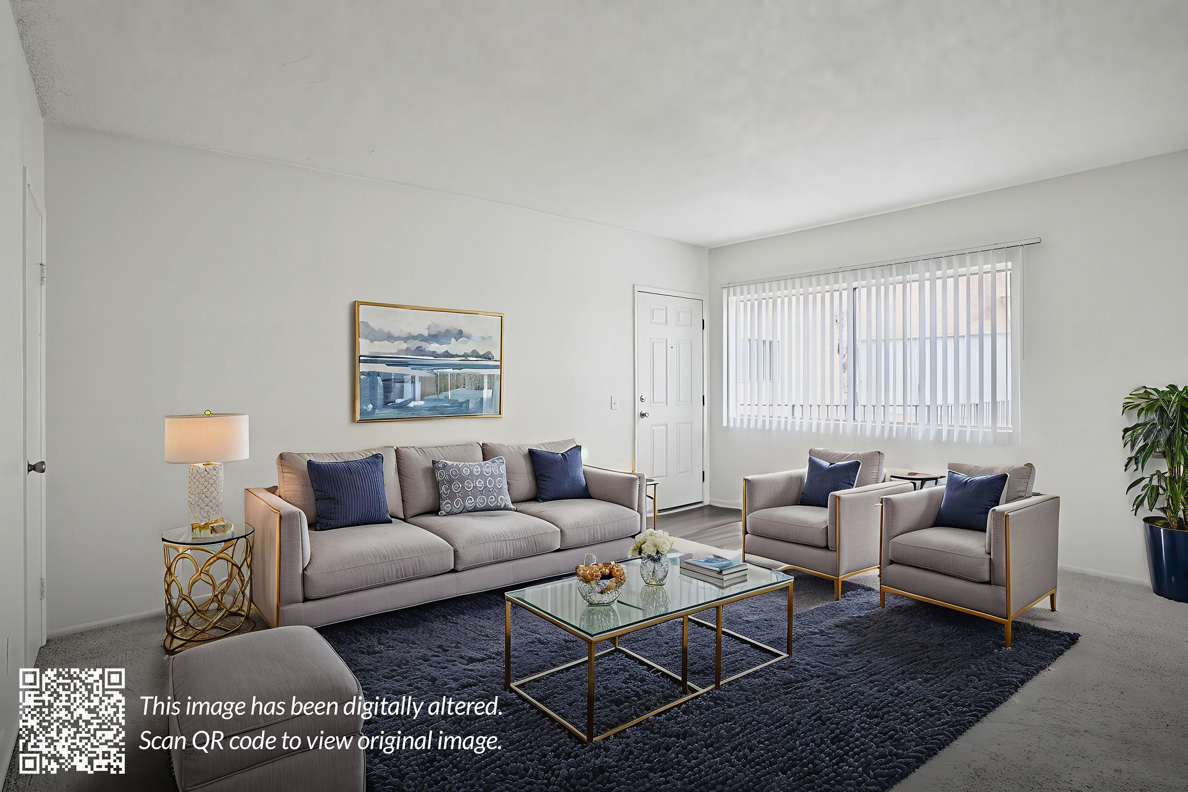 A modern living room featuring a light gray sofa with decorative pillows, two matching armchairs, and a glass coffee table on a dark rug. A piece of wall art is hung above the sofa, and a potted plant sits in the corner. Natural light comes through a window with blinds.