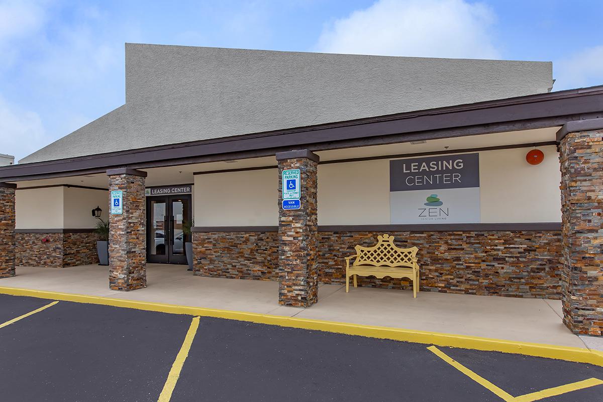 Leasing center exterior with stone pillars, yellow bench, and signage indicating the leasing center and Zen.