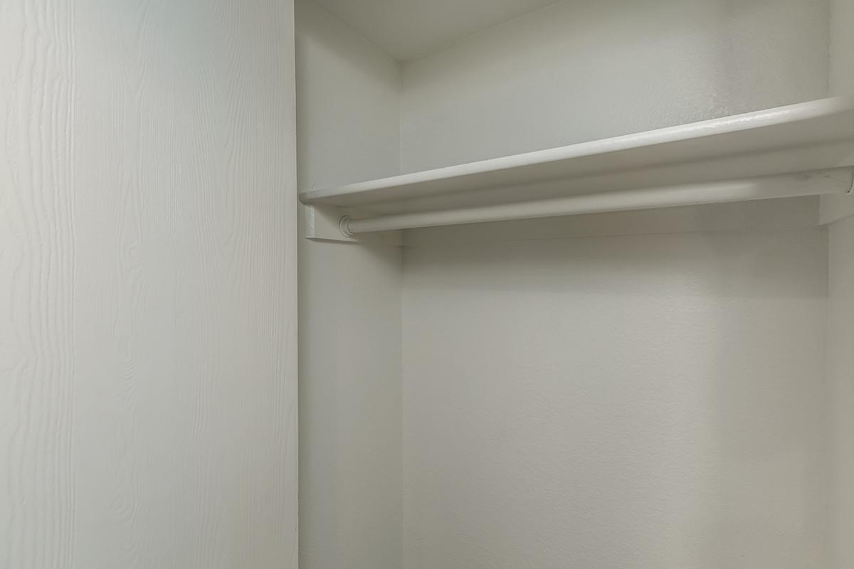 A simple, empty closet with white walls and a single horizontal shelf. The space is unadorned and minimalist, showcasing a clean and tidy appearance. The absence of items emphasizes the blankness of the storage area.