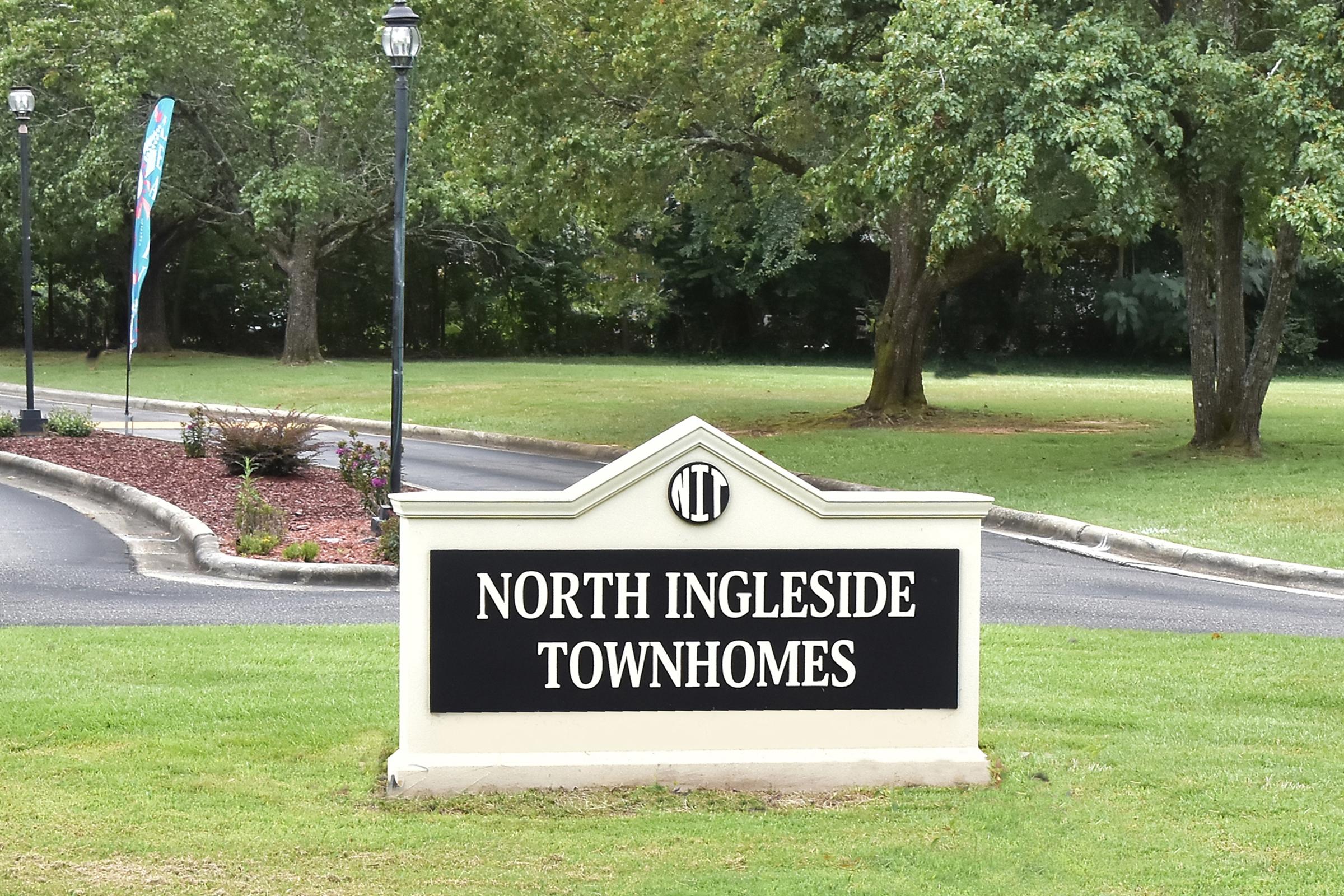 Sign for North Ingleside Townhomes, featuring the name prominently displayed in white text on a black background, surrounded by greenery and a landscaped area. The logo is visible above the text, along with decorative lanterns on either side.
