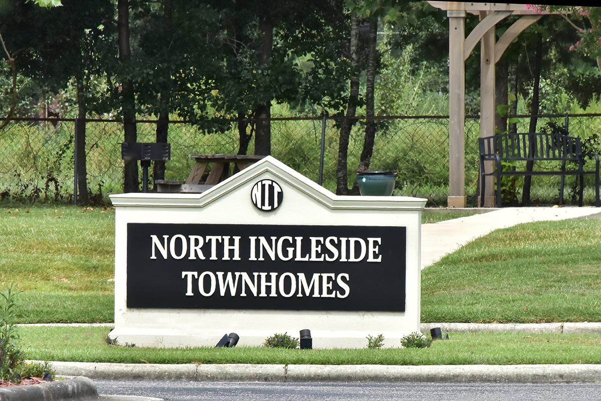 Sign for North Ingleside Townhomes, featuring the name prominently on a decorative plaque. The sign is set in a green outdoor area with well-maintained grass and nearby seating.