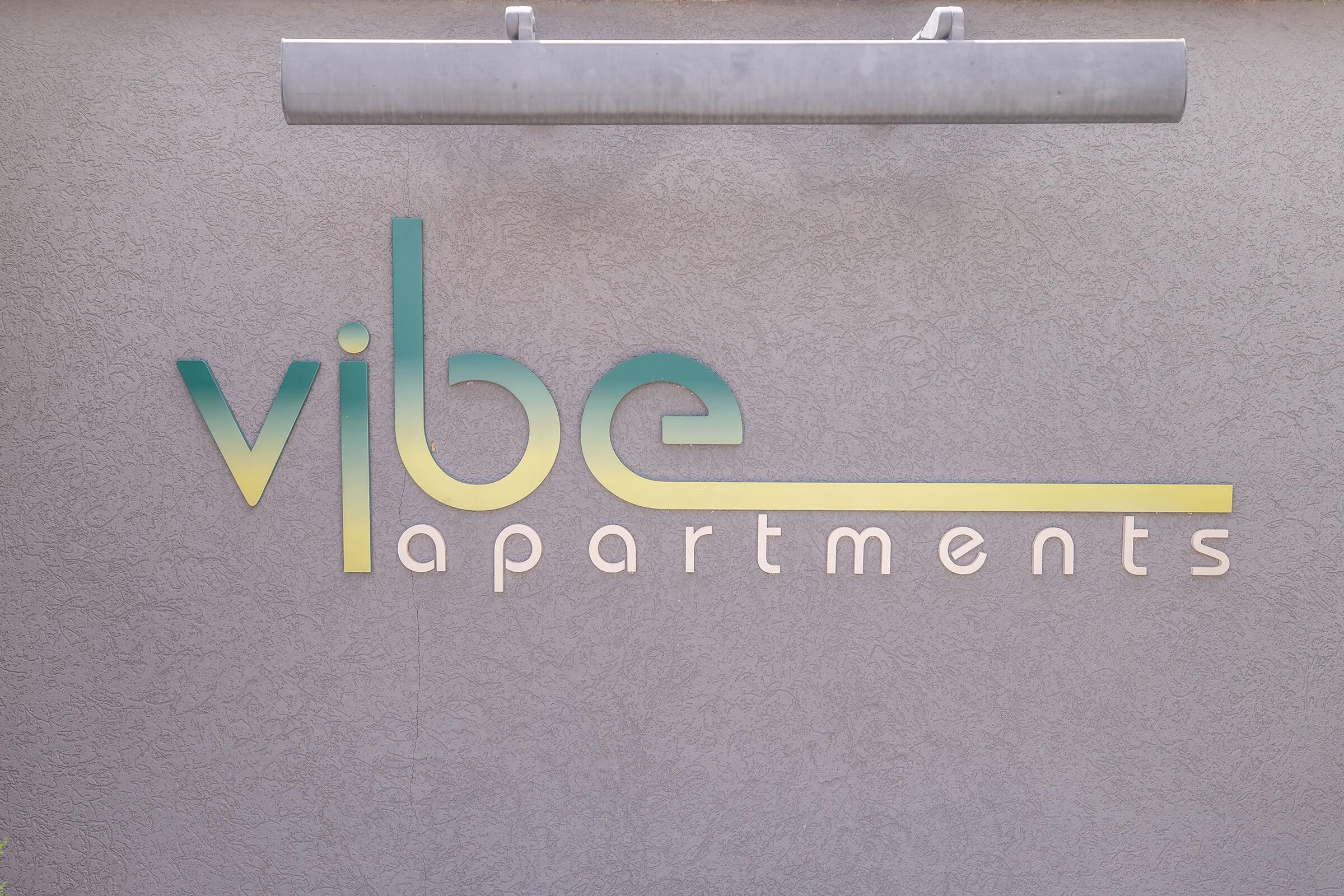 Sign for "vibe apartments" in stylized text featuring a gradient color scheme, displayed on a textured wall.