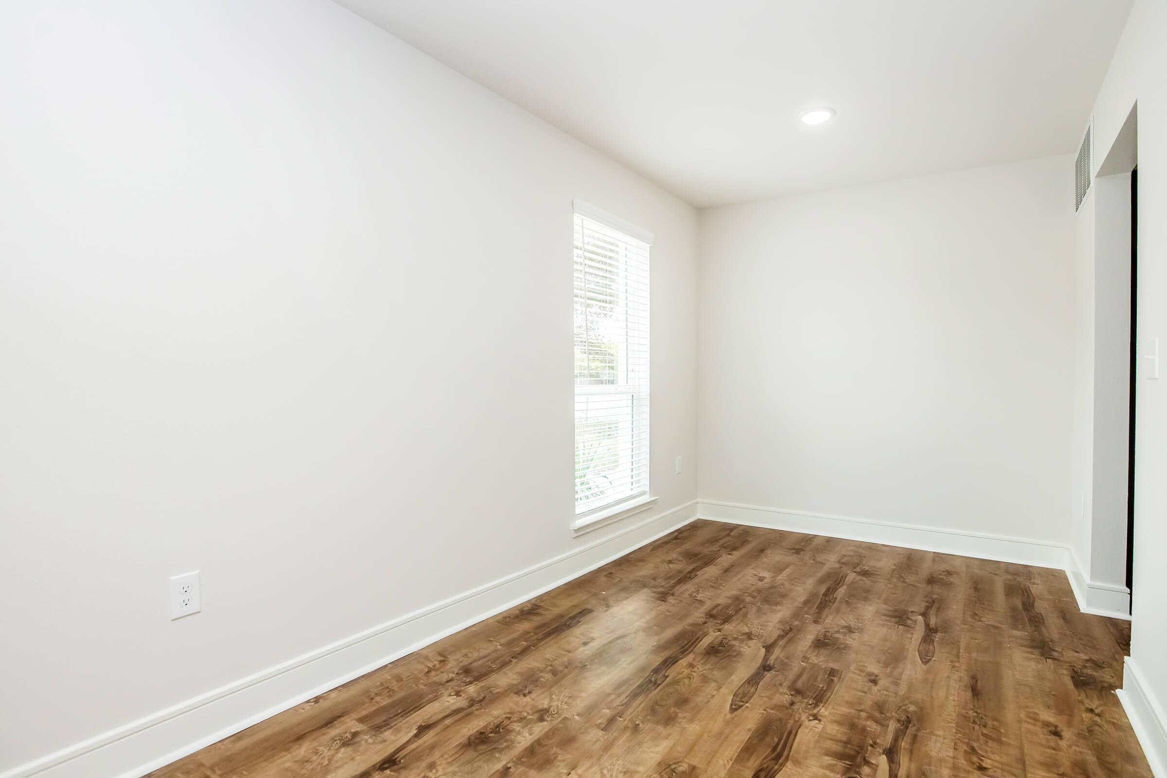 Empty room with light-colored walls and a hardwood floor. A window allows natural light to enter, creating a bright atmosphere. There’s minimal furniture or decoration, emphasizing a spacious and clean aesthetic. The overall ambiance is simple and inviting.