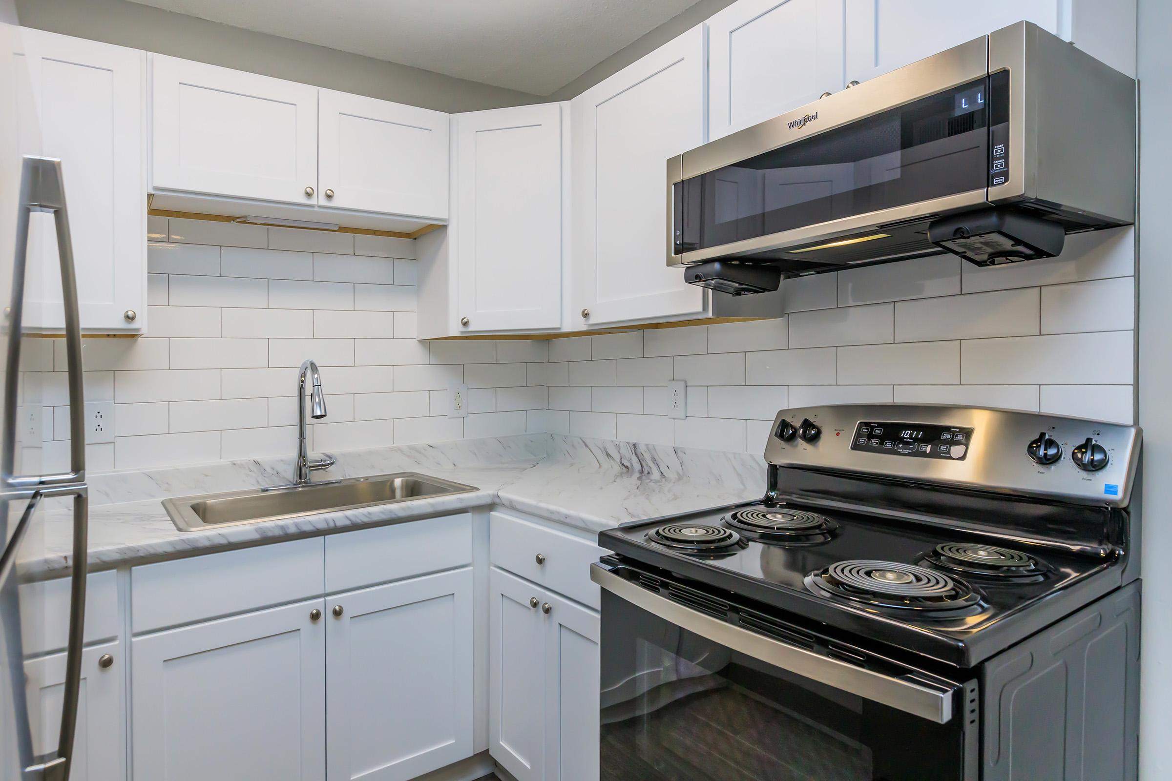 A modern kitchen featuring white cabinetry, a stainless steel refrigerator, a sleek black stove with an oven, and a stylish microwave. The countertop is made of marble, and the backsplash consists of white subway tiles, creating a clean and contemporary aesthetic.