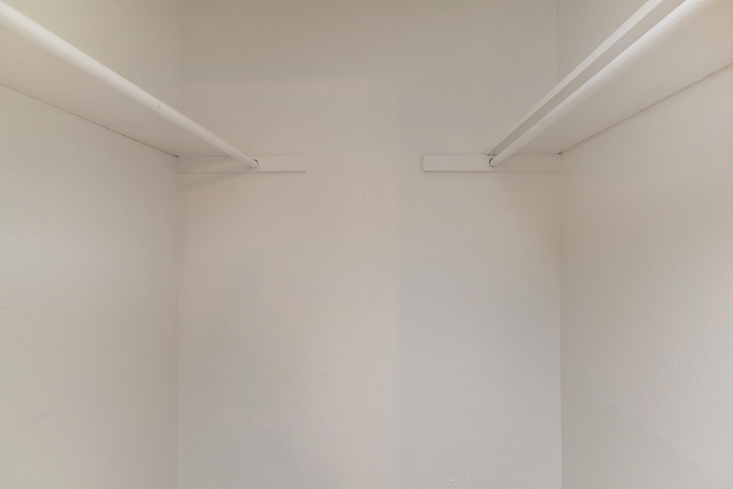 Empty closet with white walls and two horizontal hanging rods at the top. The space is uncluttered and minimalistic, providing a clear view of the interior.