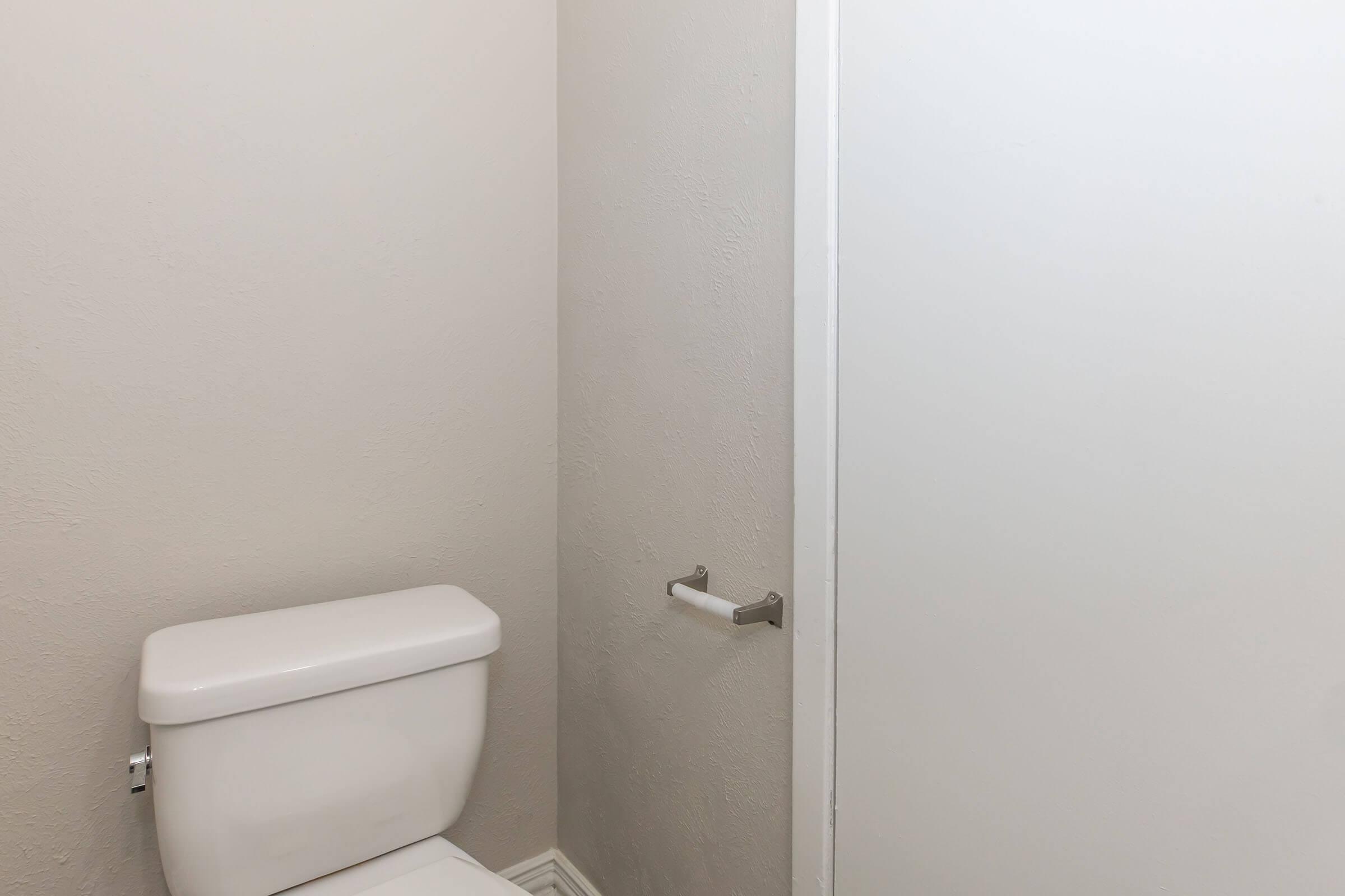 A clean and simple bathroom interior featuring a white toilet against a light gray wall, with a closed door and a towel bar nearby. The overall aesthetic is minimalist and modern.