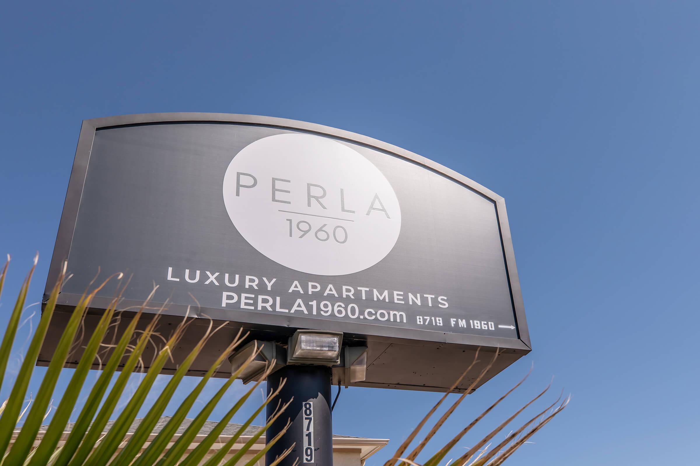 Sign for "PERLA 1960" luxury apartments, featuring the logo and website URL. The sign is set against a clear blue sky with green palm fronds in the foreground.