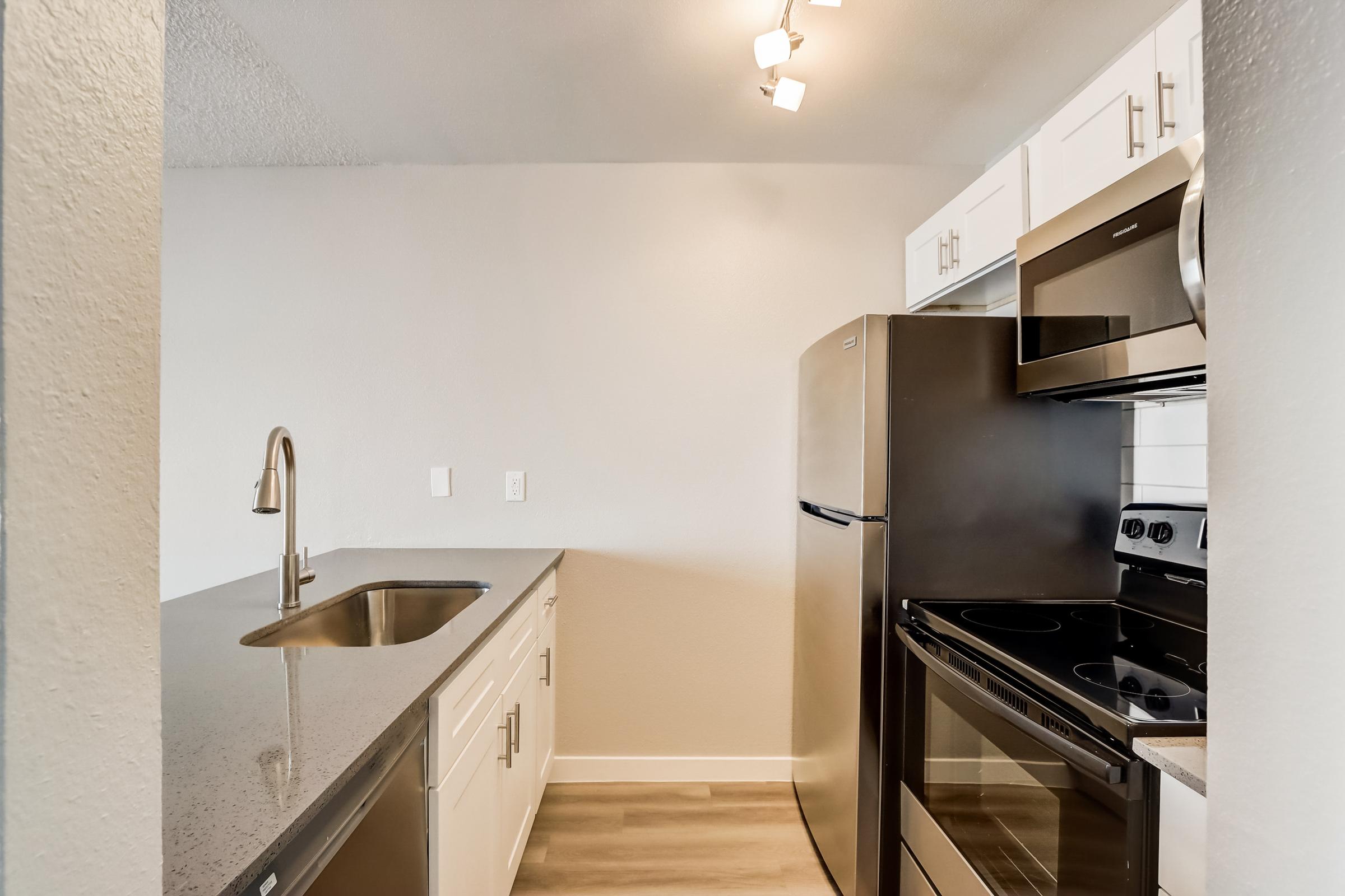 A galley kitchen with stainless steel appliances and a view of the living area at Rise at the Lofts.