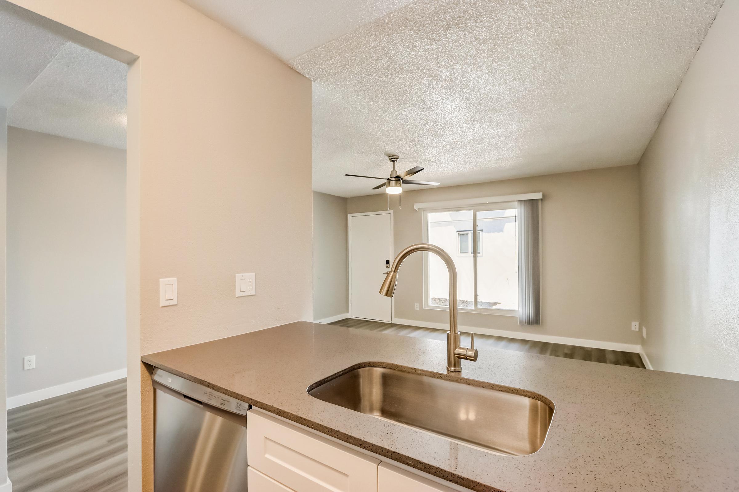 A kitchen counter with a sink looking over the living area at Rise at the Lofts. 