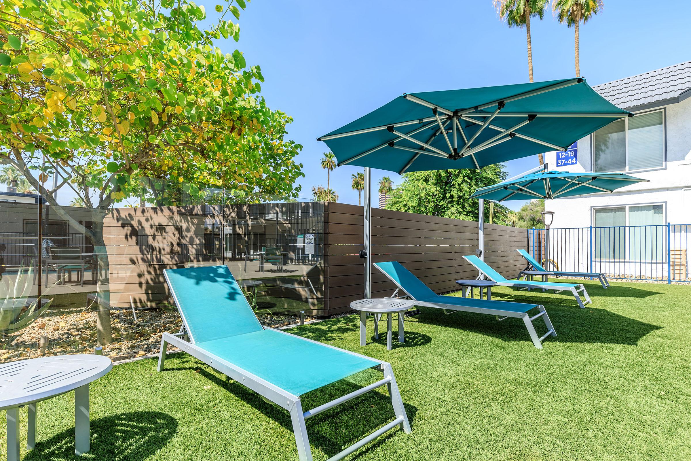 Outdoor grass area at Rise at the Lofts with tanning pool chairs and sun shade covers.