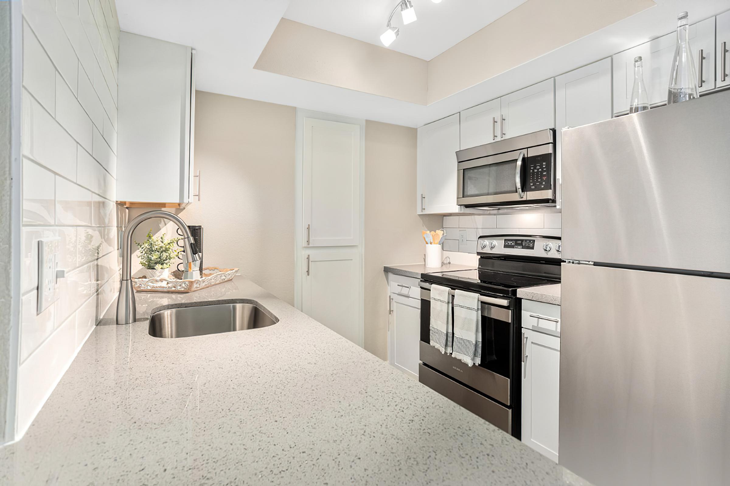 Renovated modern kitchen with stainless steel appliances, new quartz counters, and white cabinets