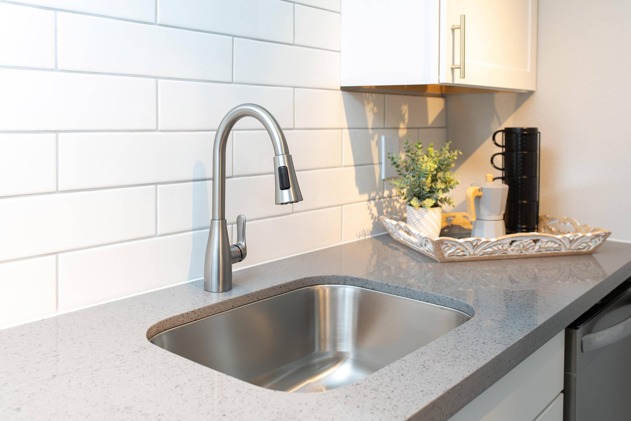 Modern stainless steel faucet and sink next to a tray of coffee supplies