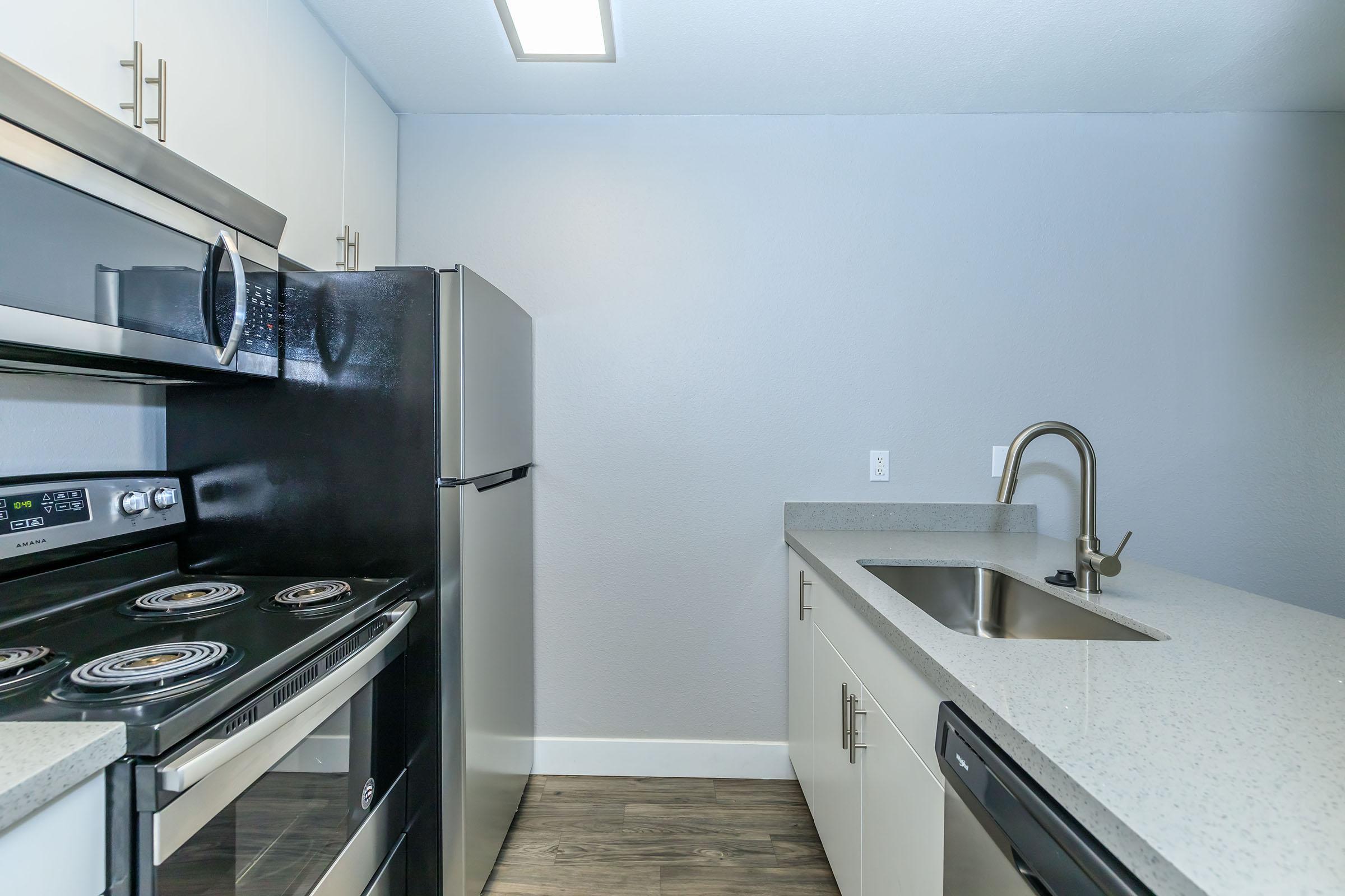 An open galley kitchen with stainless steel appliances and grey quartz countertops.