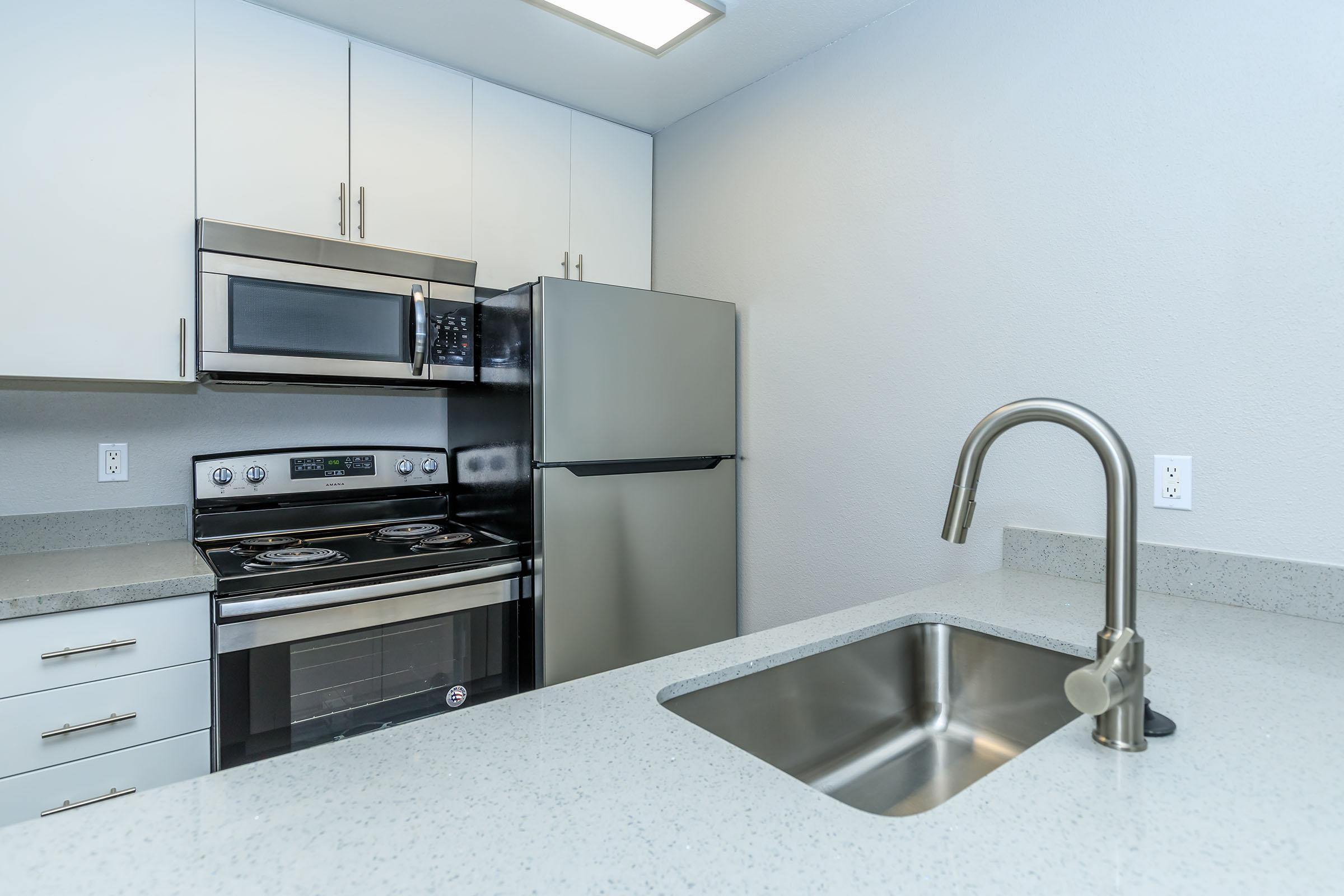 Renovated kitchen with sink built into a quartz island countertop at Rise at the Lofts. 