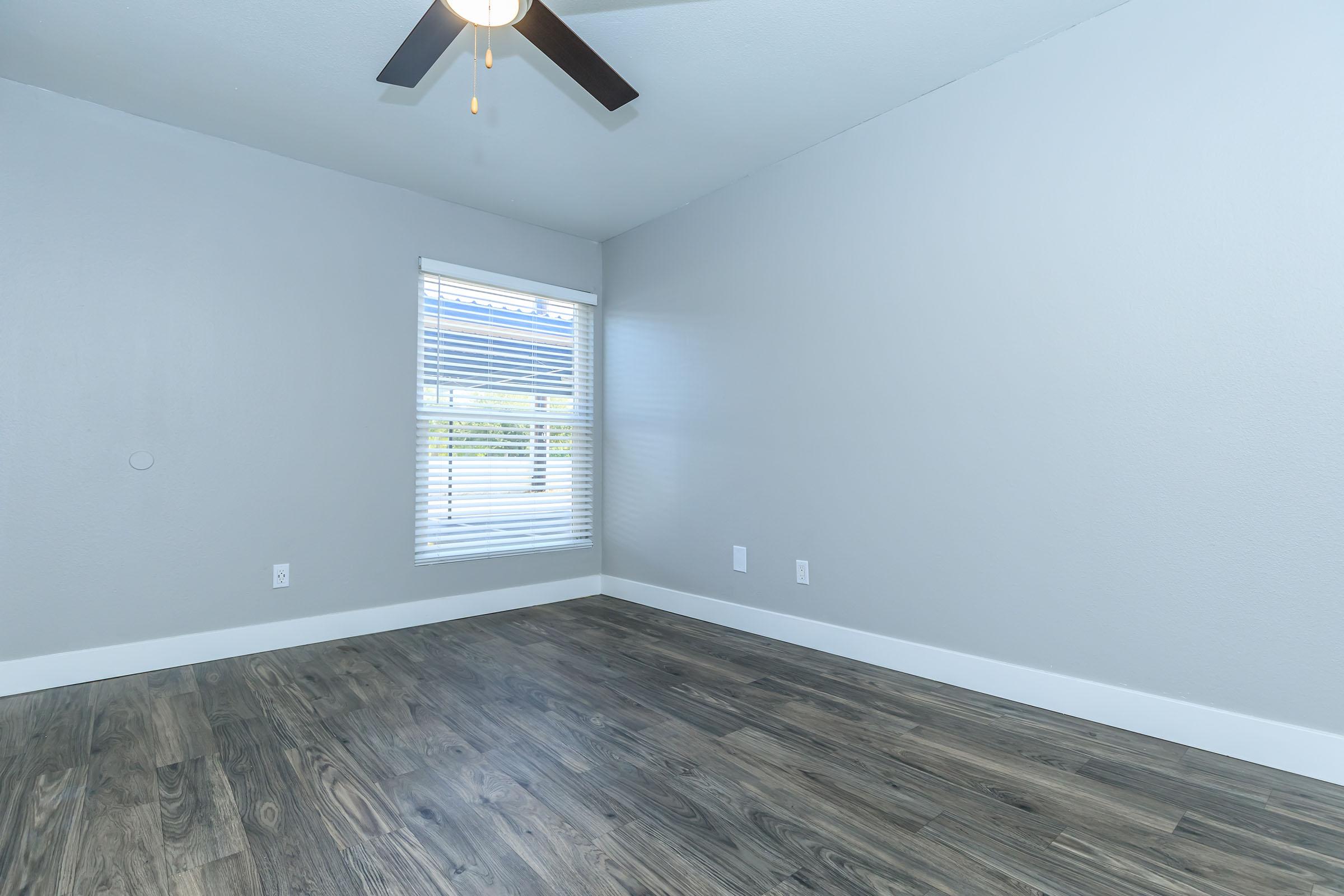 Large main bedroom with brown wood flooring, window, and ceiling fan