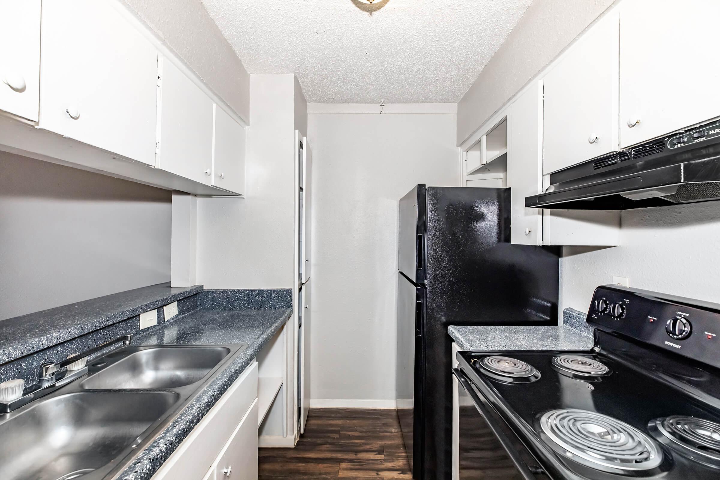 A clean, modern kitchen featuring white cabinets, dark blue countertops, a black refrigerator, and an electric stove. The space is well-lit with neutral-colored walls, showcasing an organized and functional layout ideal for cooking and meal preparation.